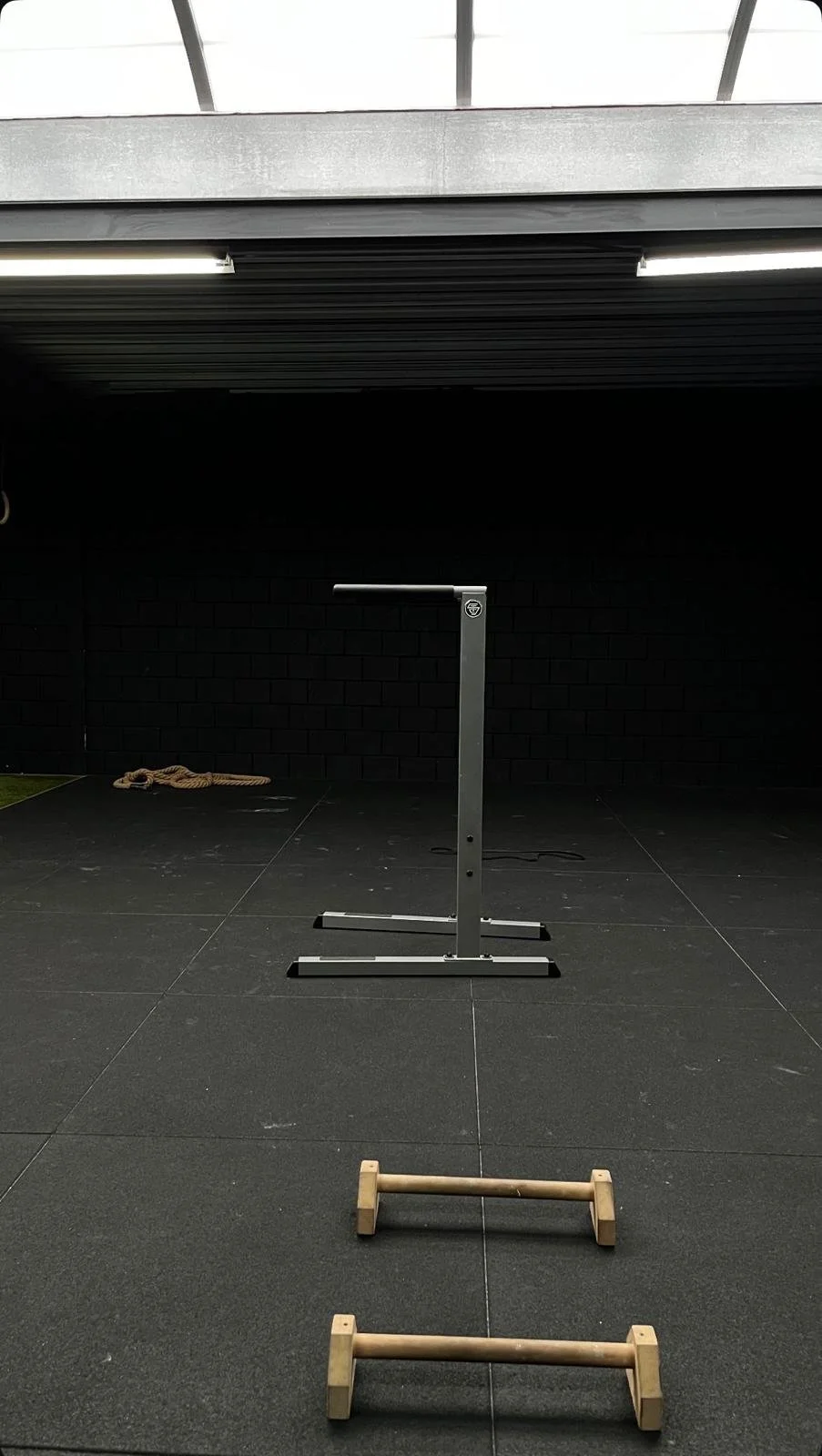 Empty indoor gym space with black rubber flooring, Dip station and two wooden push-up bars on the floor.