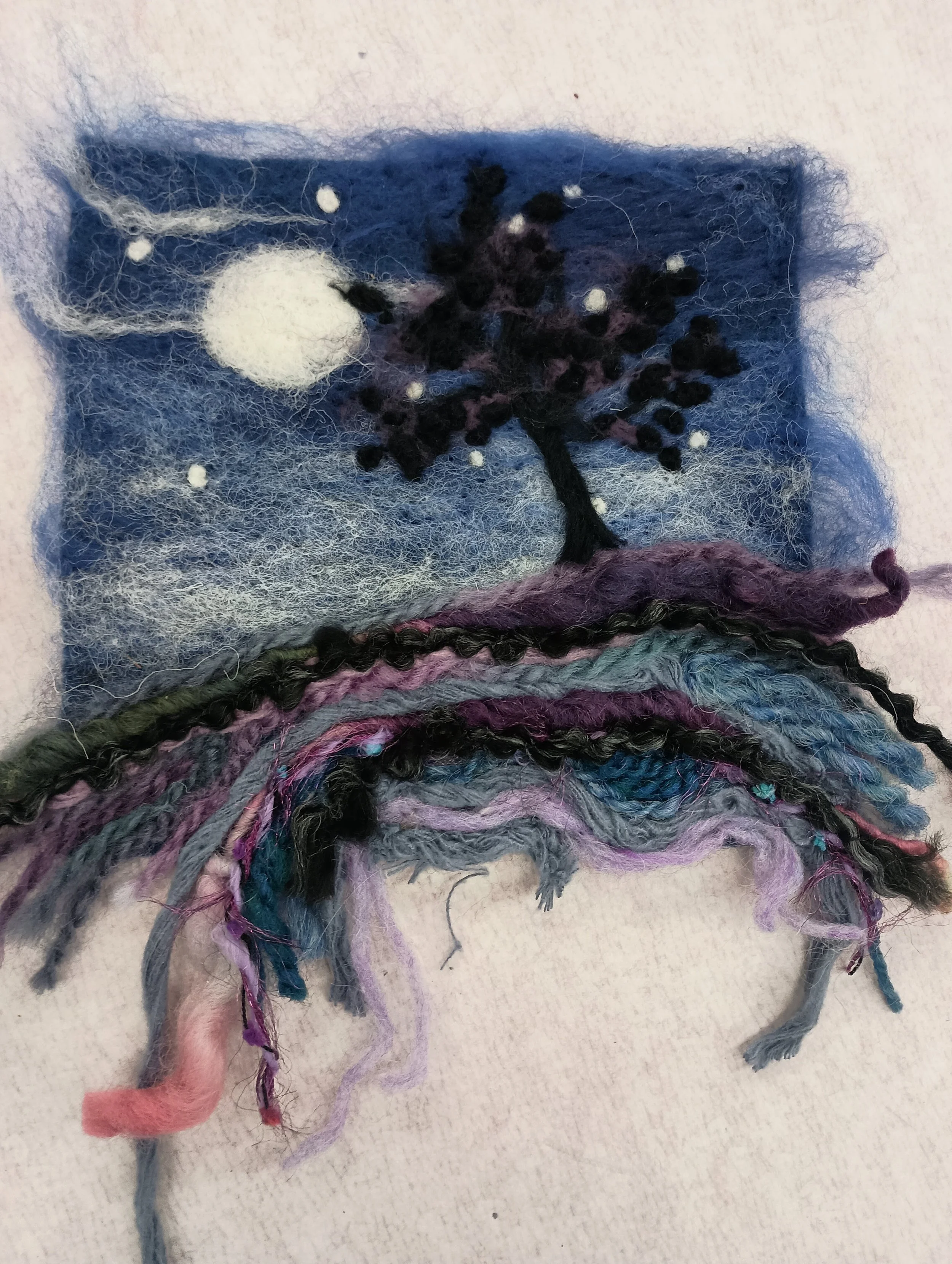 Felted artwork of a moonlit night scene with a tree and falling snow, with colorful yarn strands below.
