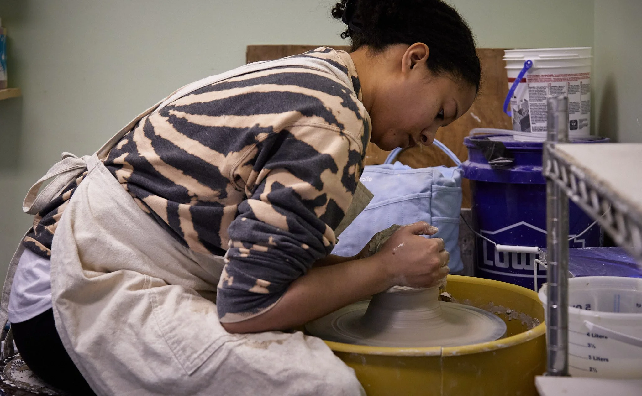 A person shaping clay on a pottery wheel in a studio.