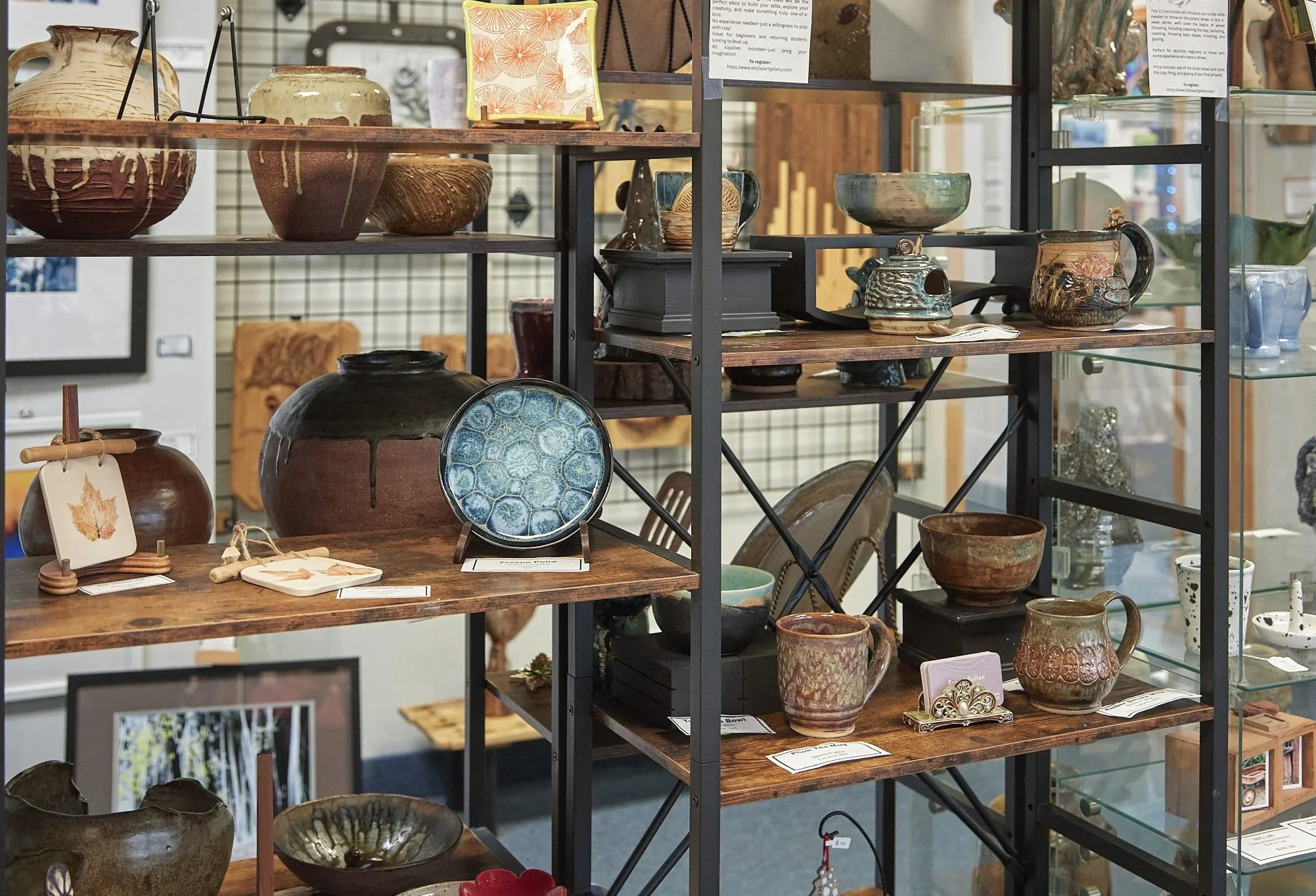 Display of various ceramic pottery and decorative items on wooden and glass shelves, including bowls, vases, and mugs, in an antique or craft store.