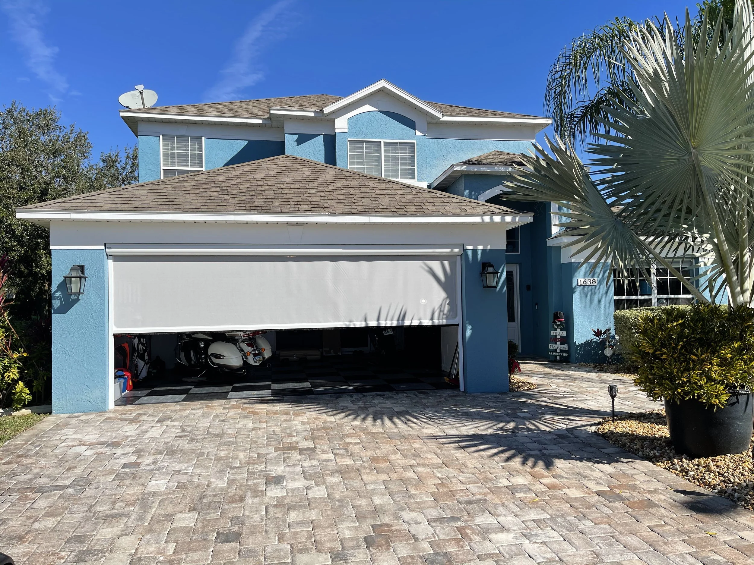Blue two-story house with a garage, palm trees, and a paved driveway.
