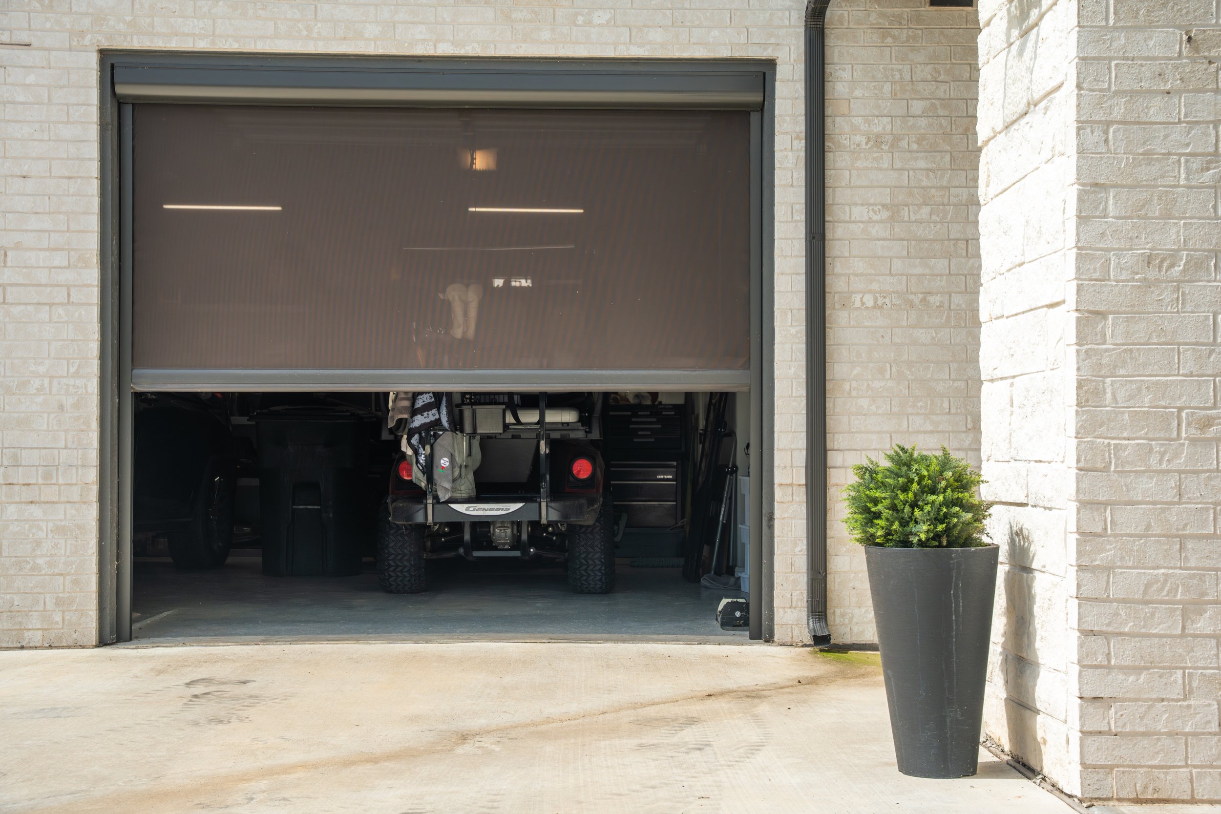 Garage door partially open revealing a golf cart inside, with a large potted plant outside on the right.
