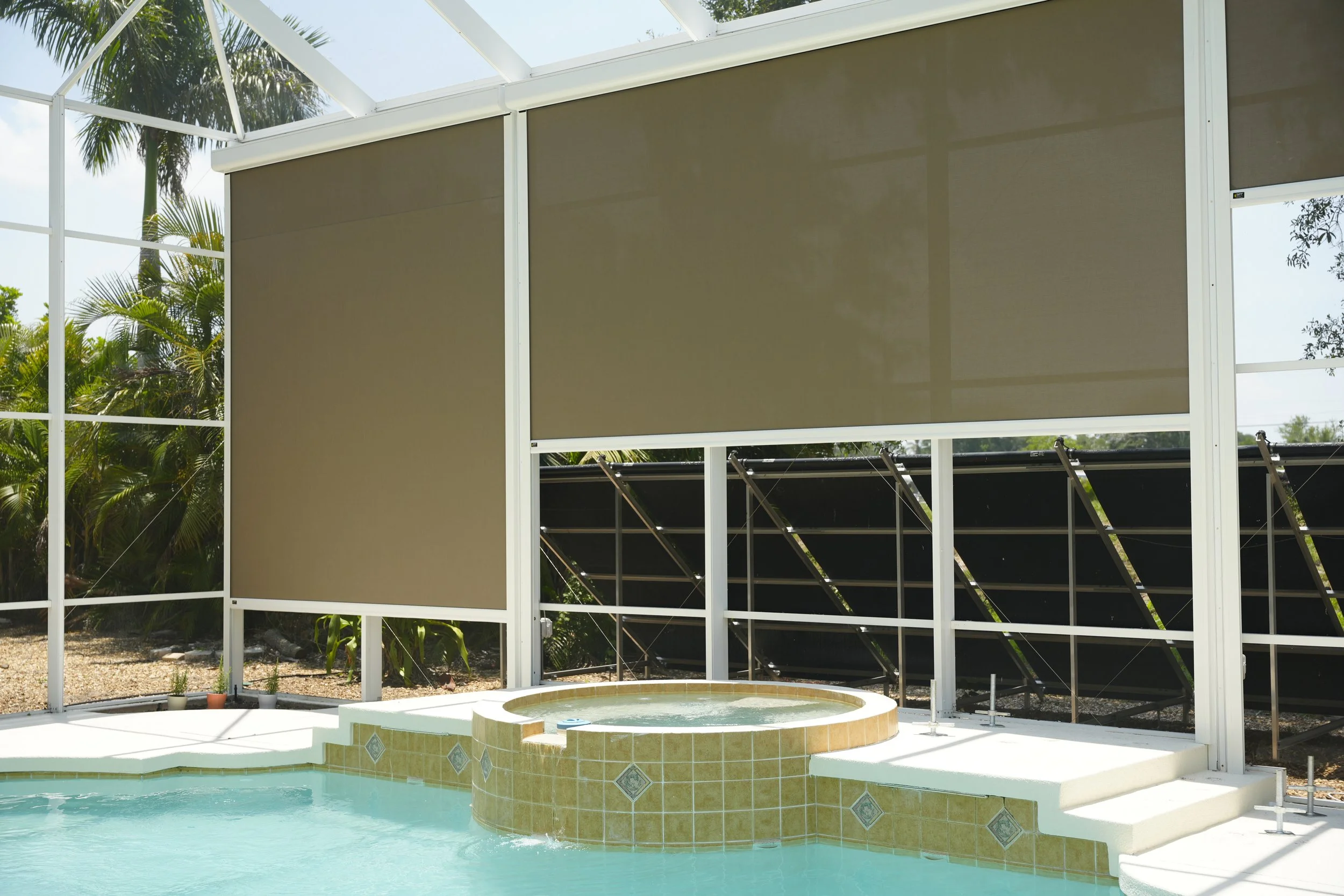 Pool area with hot tub and screen enclosure, tropical plants outside.