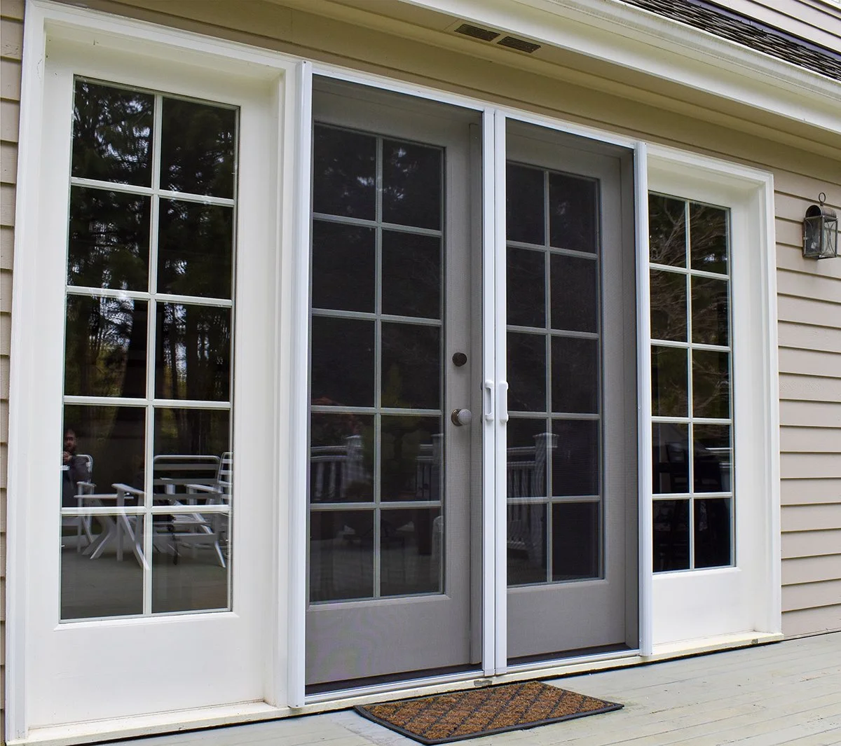 Exterior view of a house with a sliding glass door and sidelights, through which outdoor furniture is visible.