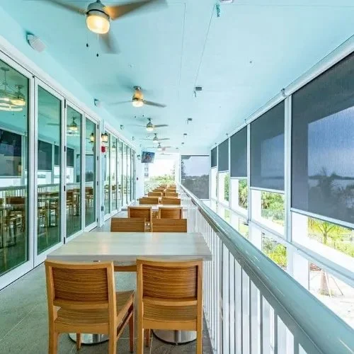 Empty outdoor balcony with seating, glass doors, and window blinds, overlooking a green landscape.