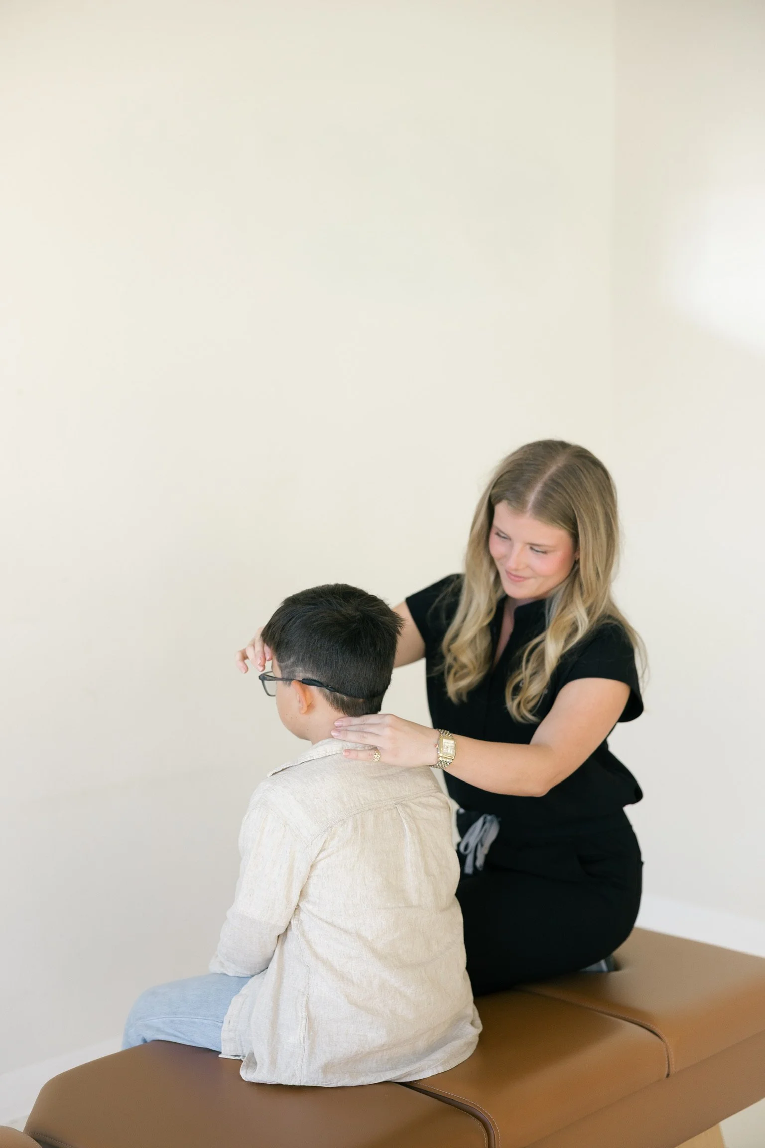A woman providing a therapeutic or medical treatment to a young boy seated on a brown bench in a clinical setting.