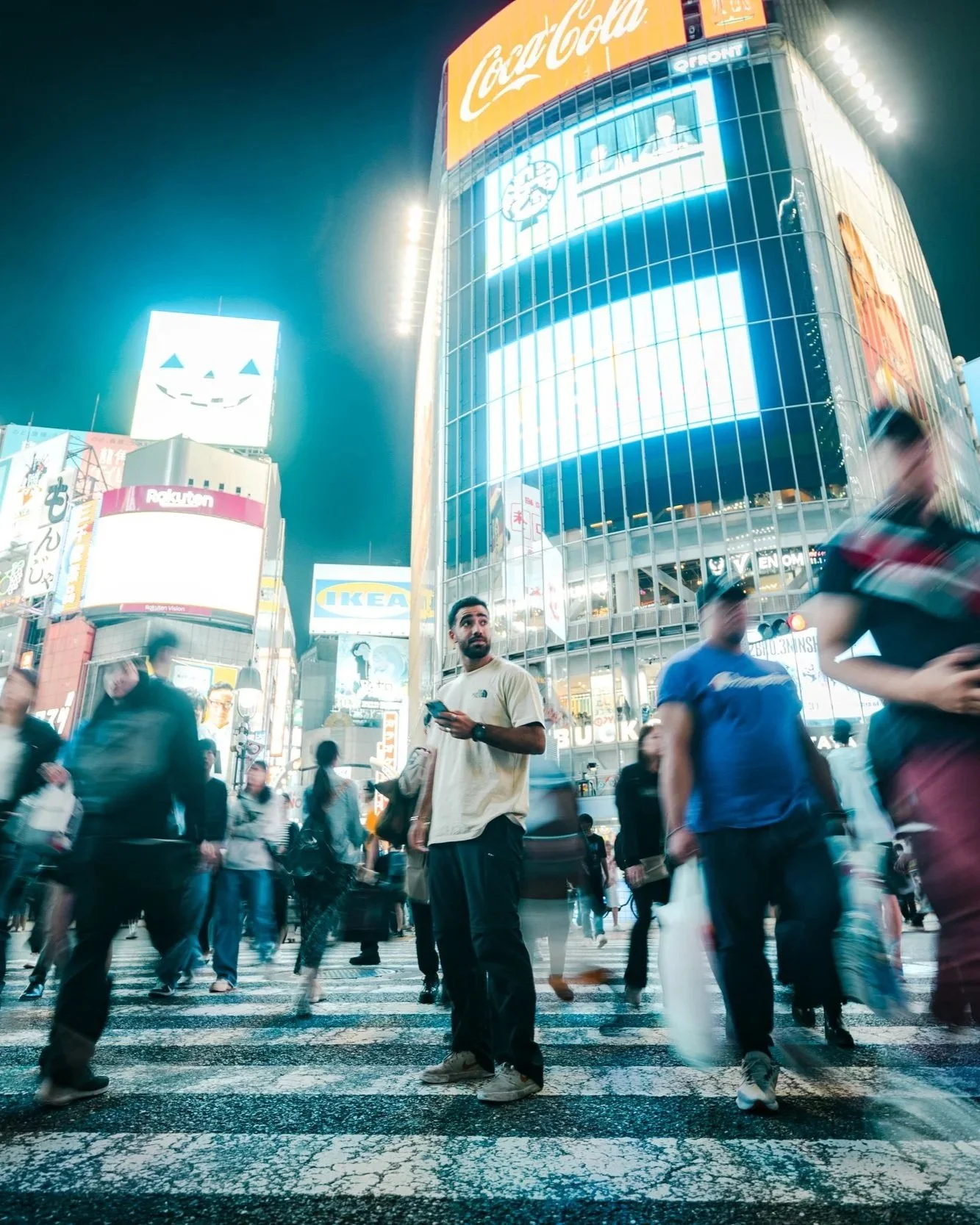 Nighttime scene of Times Square with illuminated billboards and a crowd of pedestrians crossing the street, some blurred due to motion.