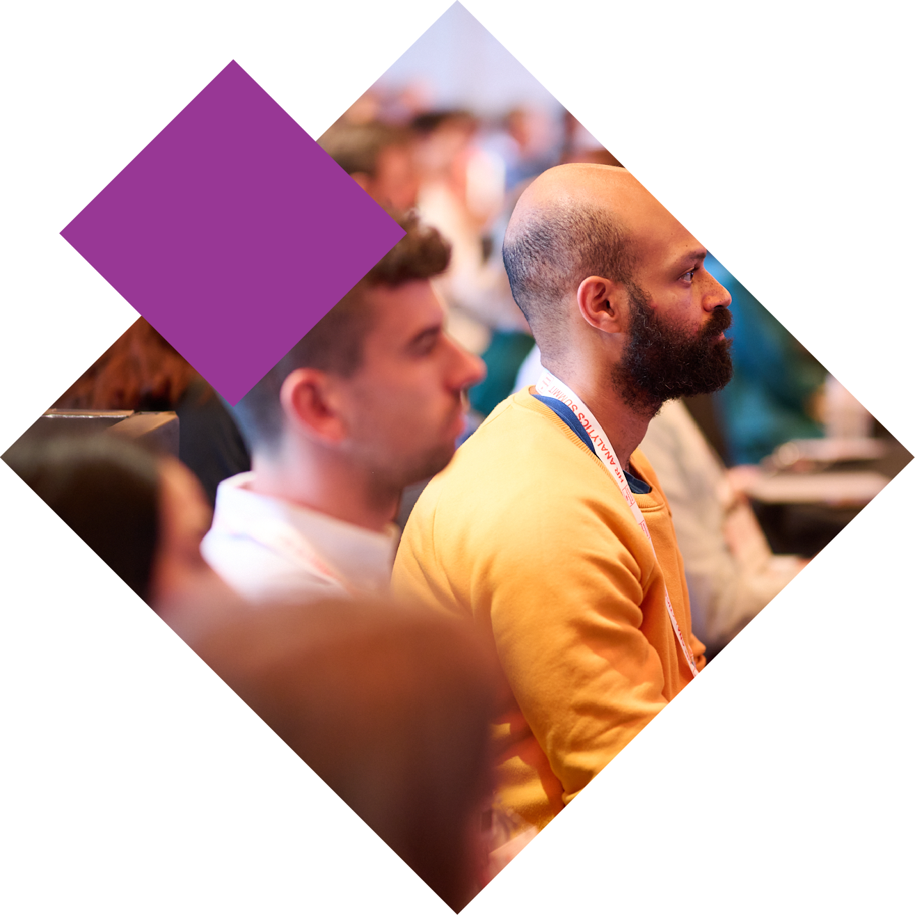 Audience at a conference, man in yellow shirt listening attentively, diamond shape overlay.