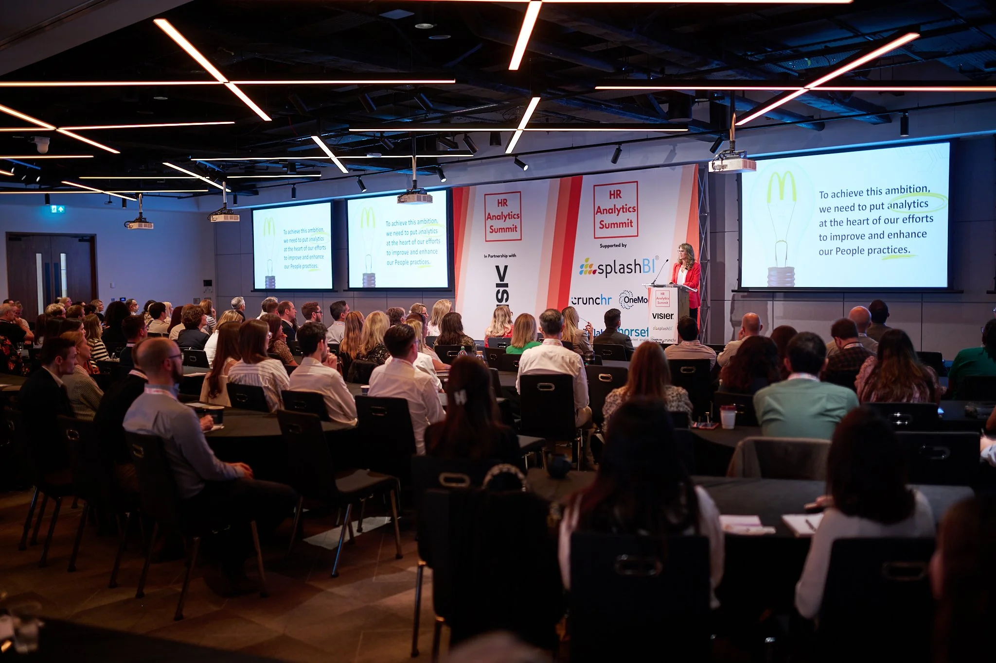 Conference attendees seated facing a speaker at the HR Analytics Summit, with presentation slides on the screen.