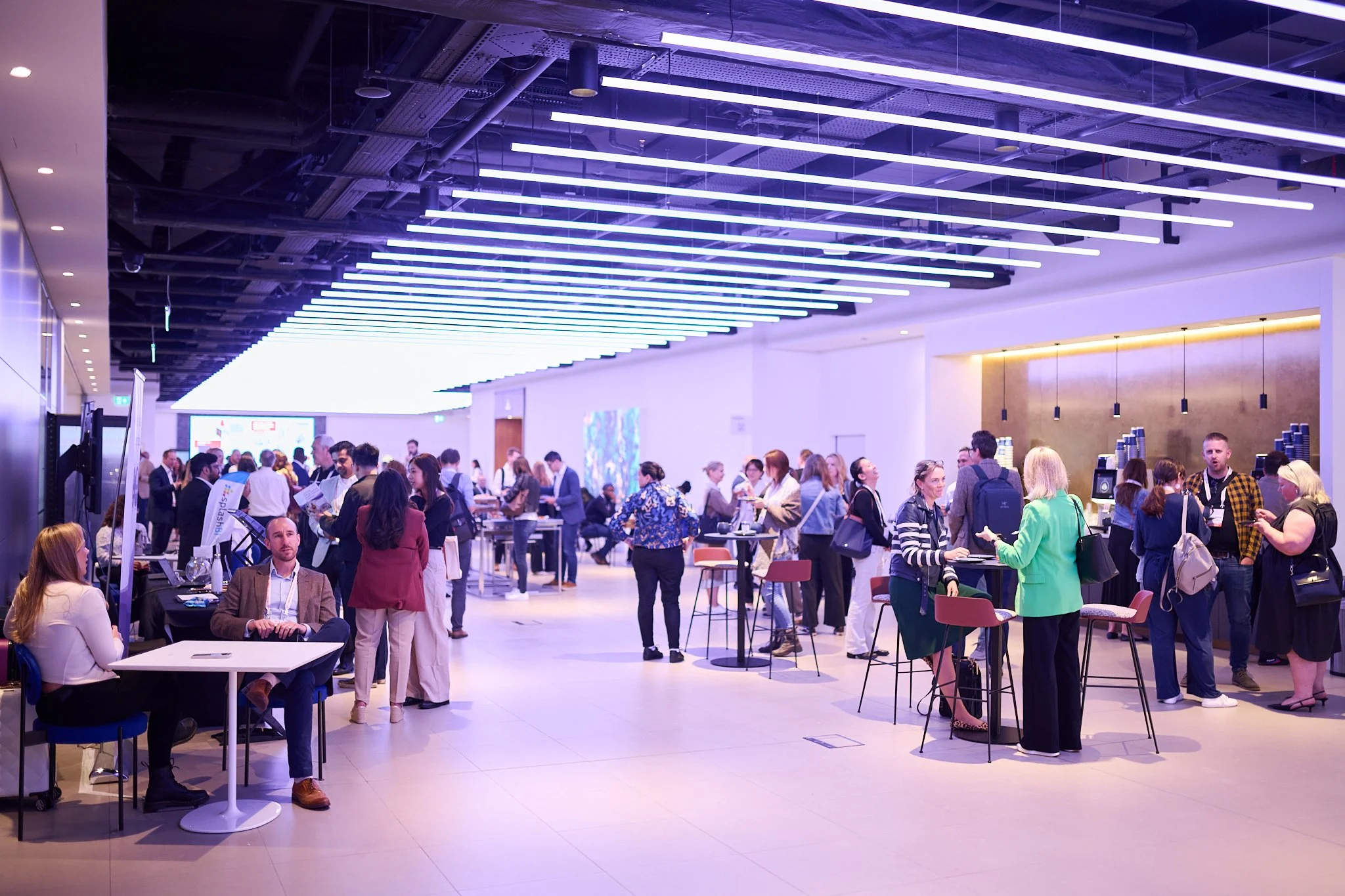 Networking event with attendees in a modern, well-lit venue, featuring tables and seating areas.