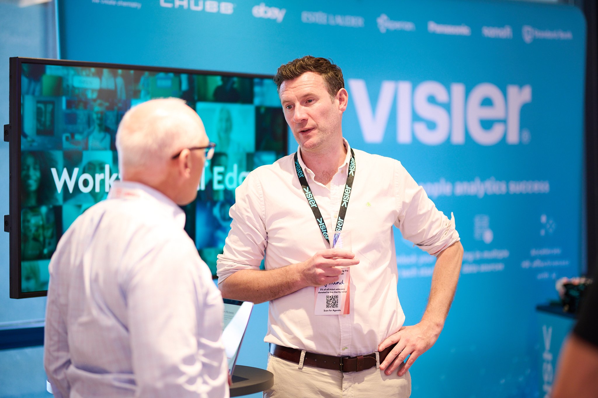 Two men talking at a Visier analytics booth at a conference or event.