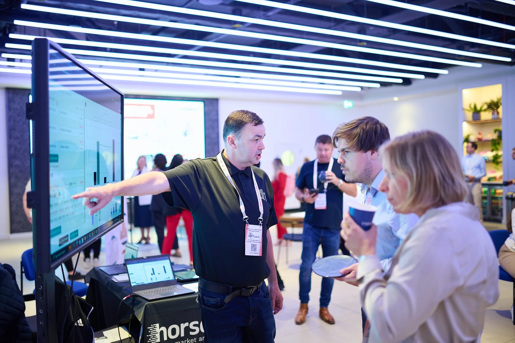 People gathered around a digital display at an event, one person pointing at the screen.