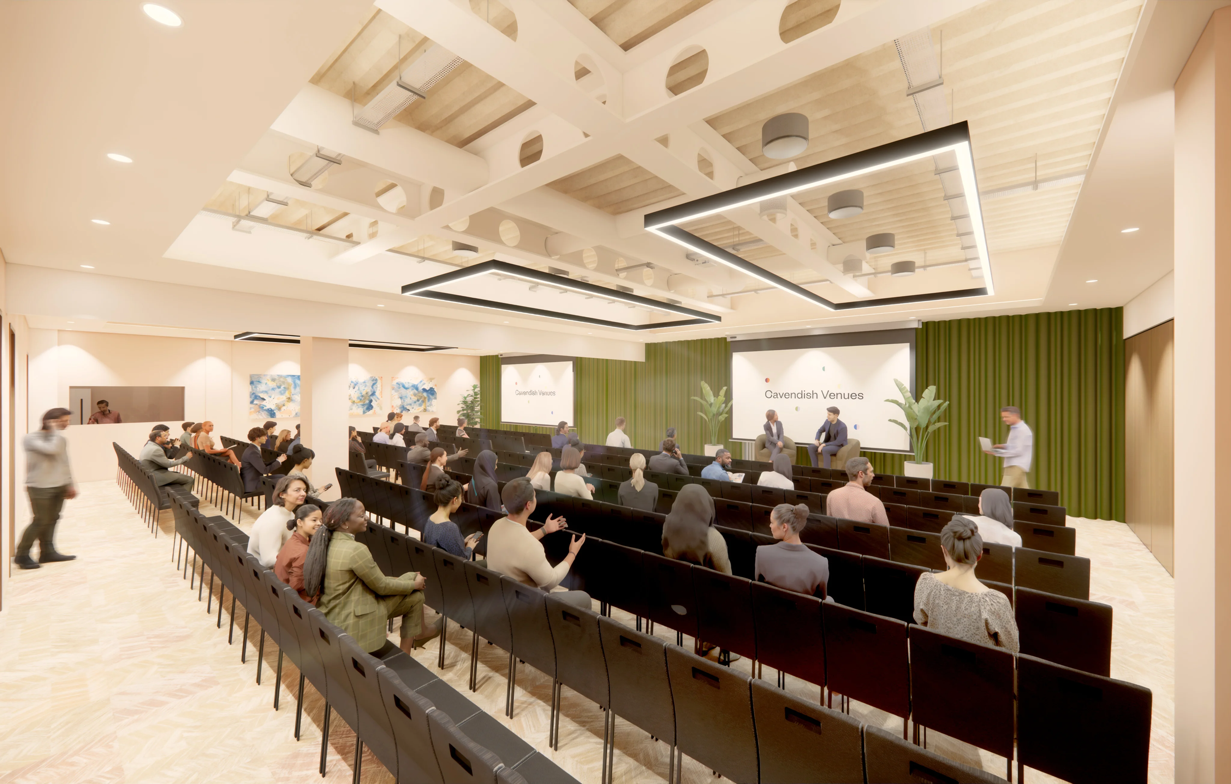A conference room with many people seated and some standing, listening to a presentation on stage with two speakers sitting and a large screen displaying the text "Cavendish Venues." The room has a high ceiling with modern lighting, green curtains be