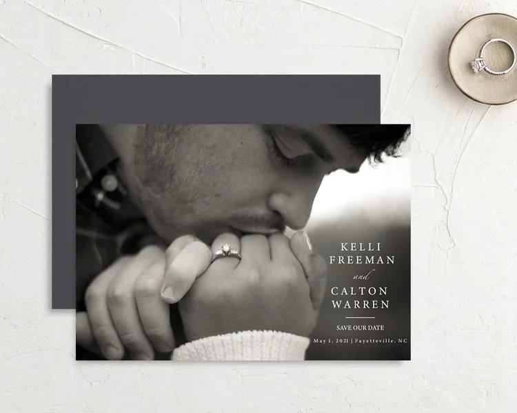 Black and white close-up of a man holding a woman's hand, both wearing rings, with text indicating a wedding save-the-date invitation for Kelli Freeman and Calton Warren, dated May 1, 2021, in Fayetteville, NC.