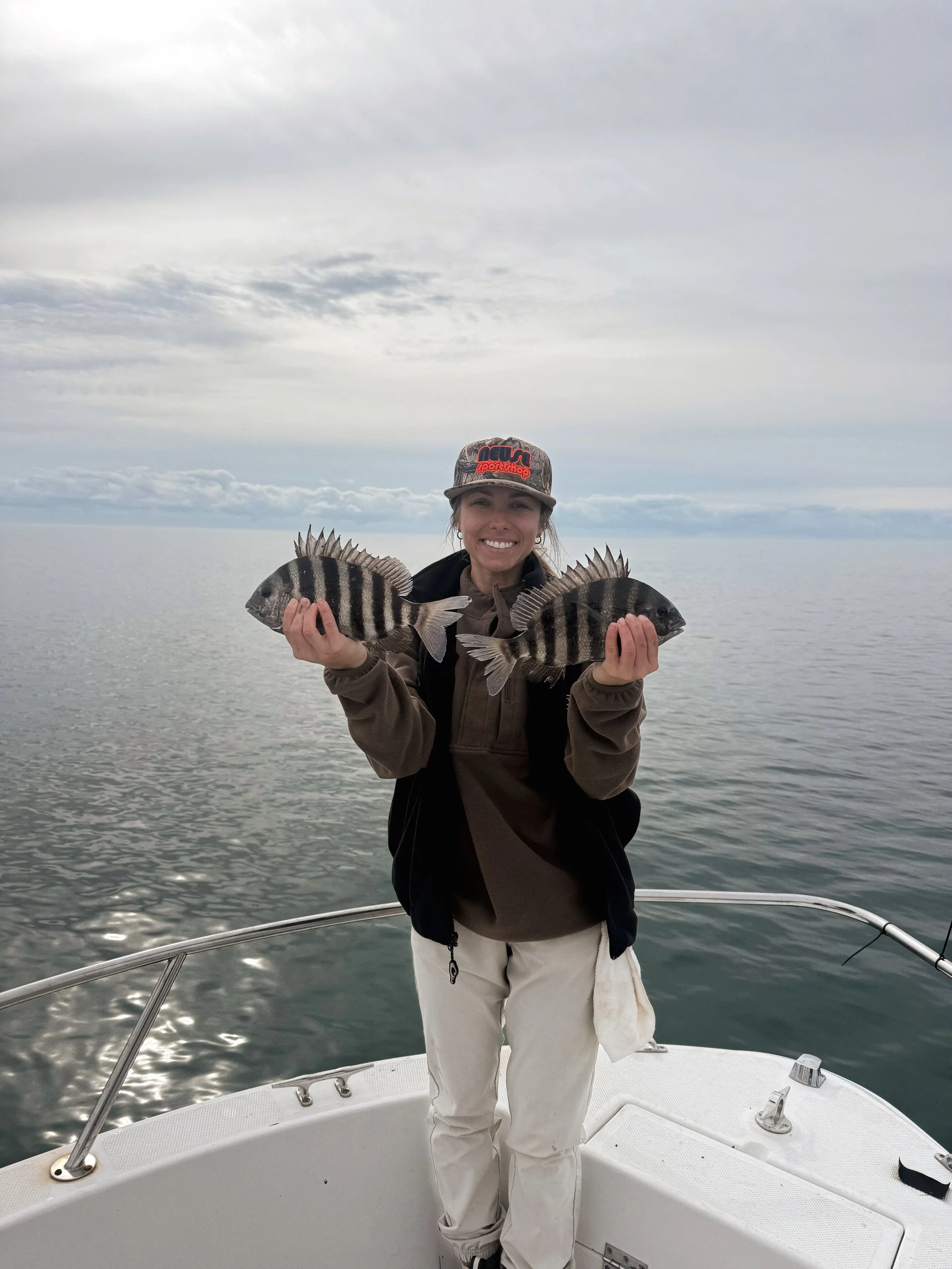 A woman holding two striped fish on a boat with an ocean and cloudy sky in the background.
