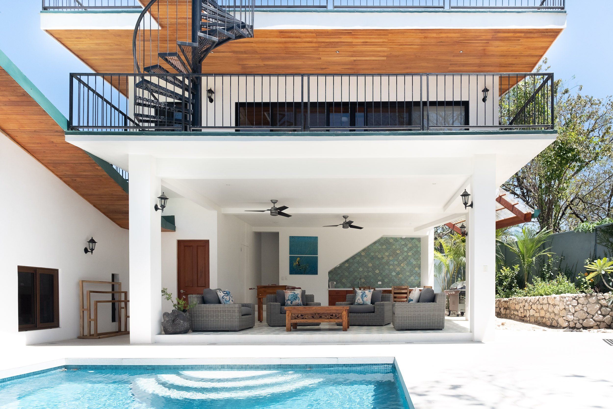 Modern house with a swimming pool, outdoor seating area, and upper balcony with spiral staircase.
