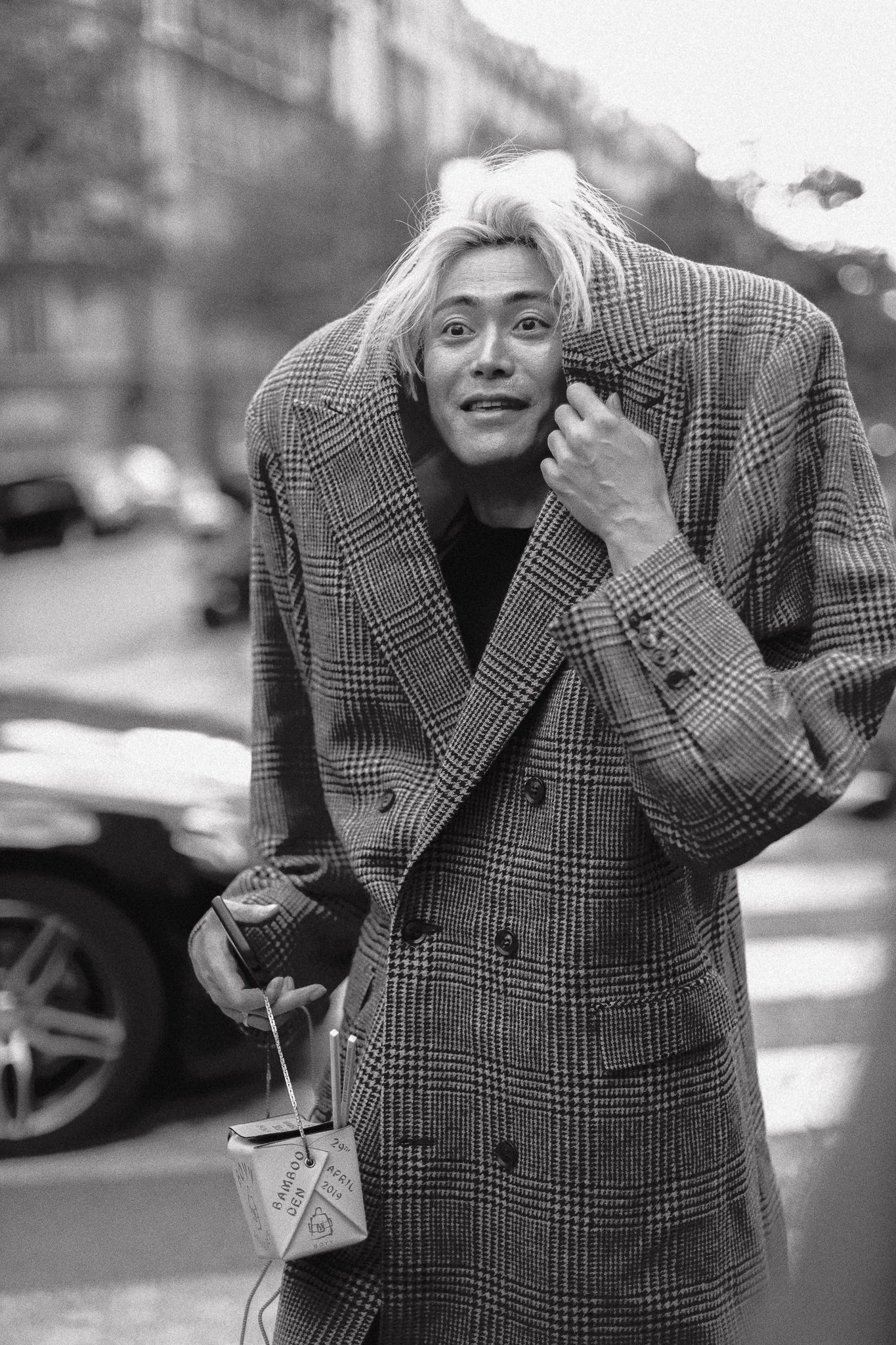 Uomo con capelli biondi ossigenati e giacca a quadri in strada, che sembra sorpreso o confuso.