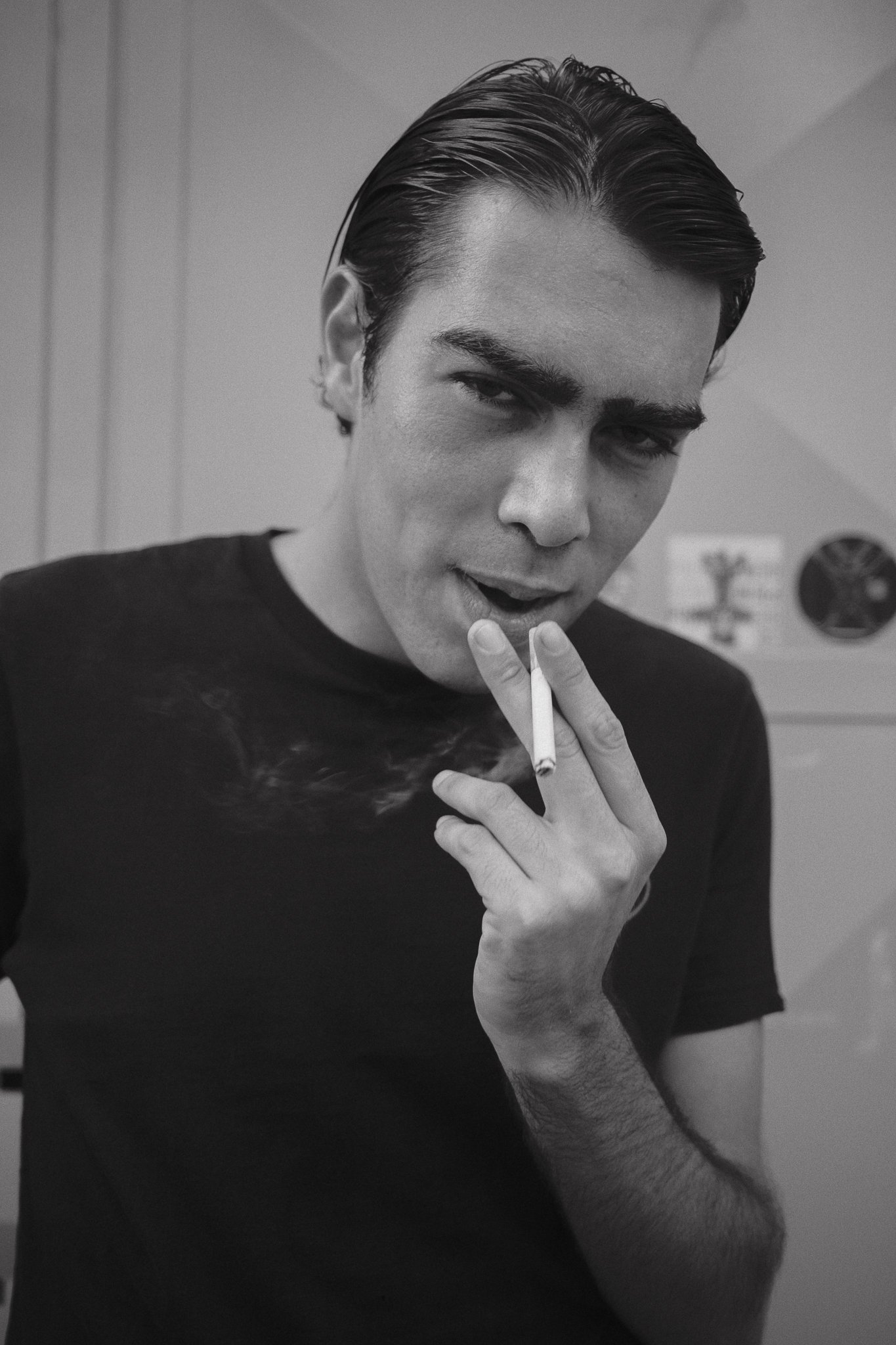 Un giovane uomo con i capelli lisci, vestito di nero, che fuma una sigaretta.