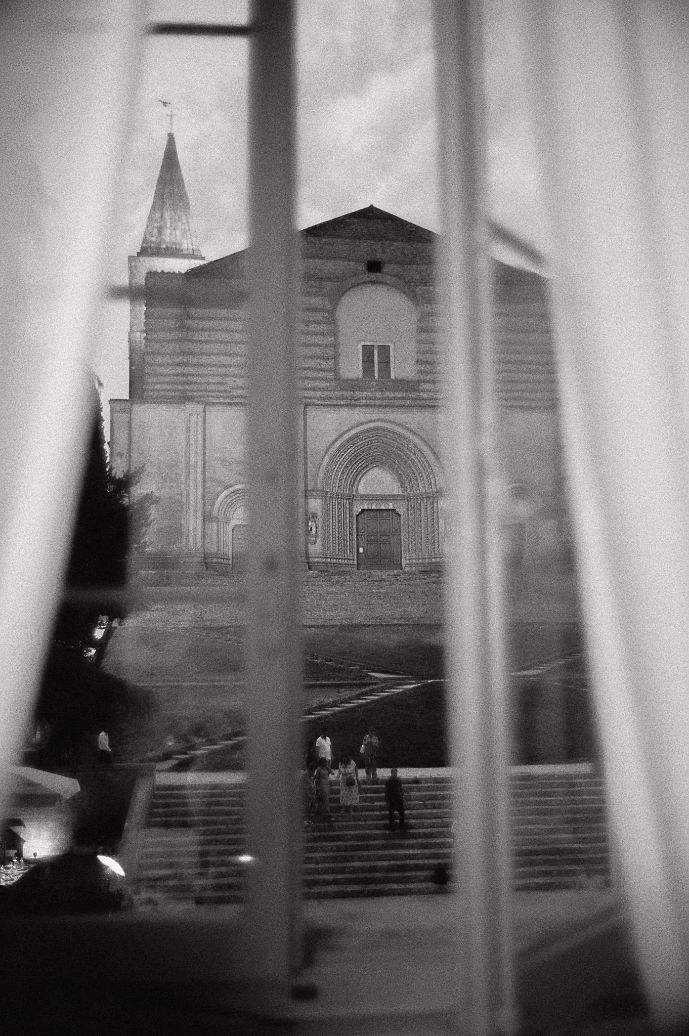 Immagine in bianco e nero di una chiesa vista attraverso una finestra con persiane
