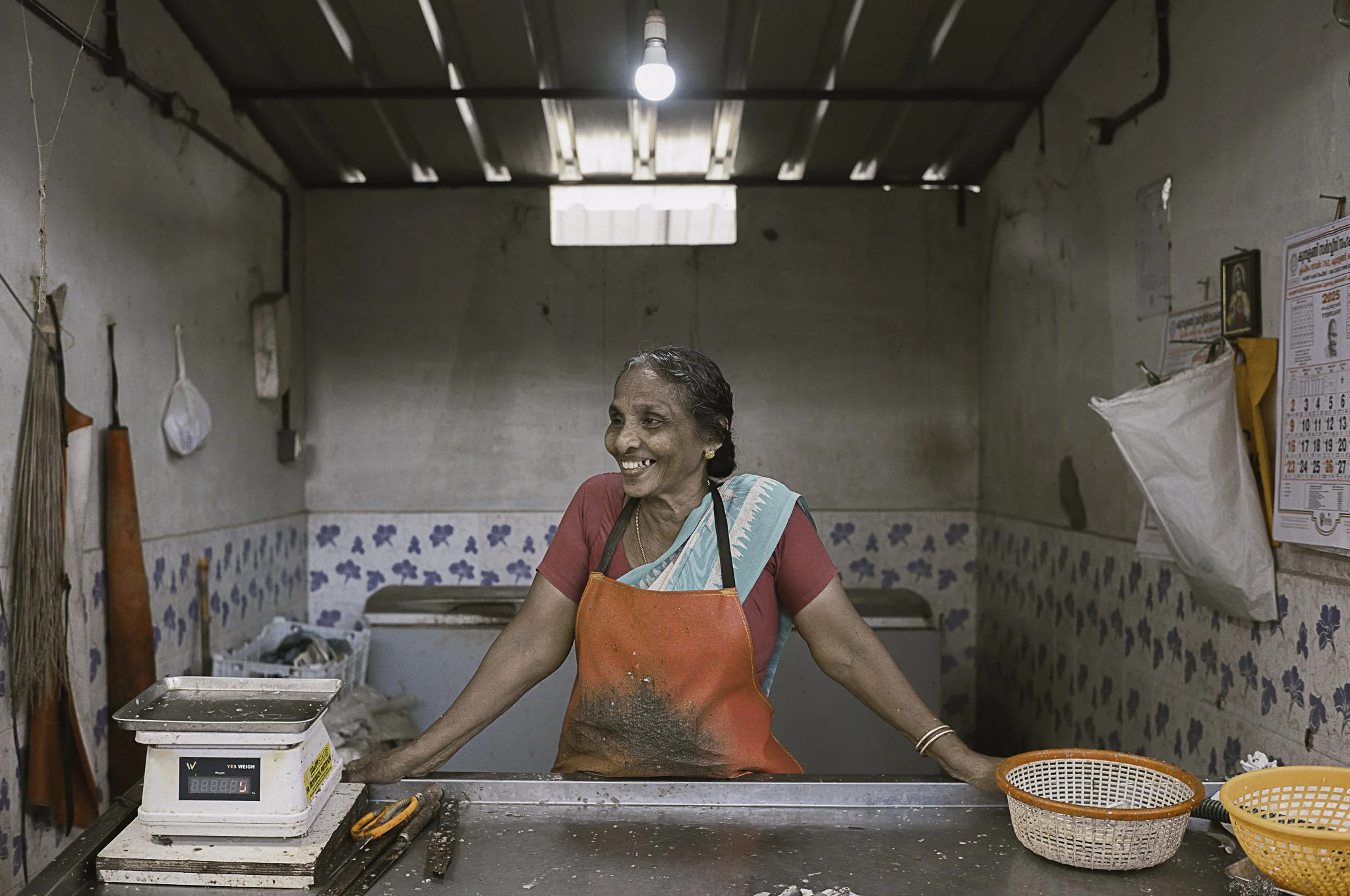 Donna anziana sorridente con grembiule rosso in un negozio o mercato, che sorride e si appoggia su un banco