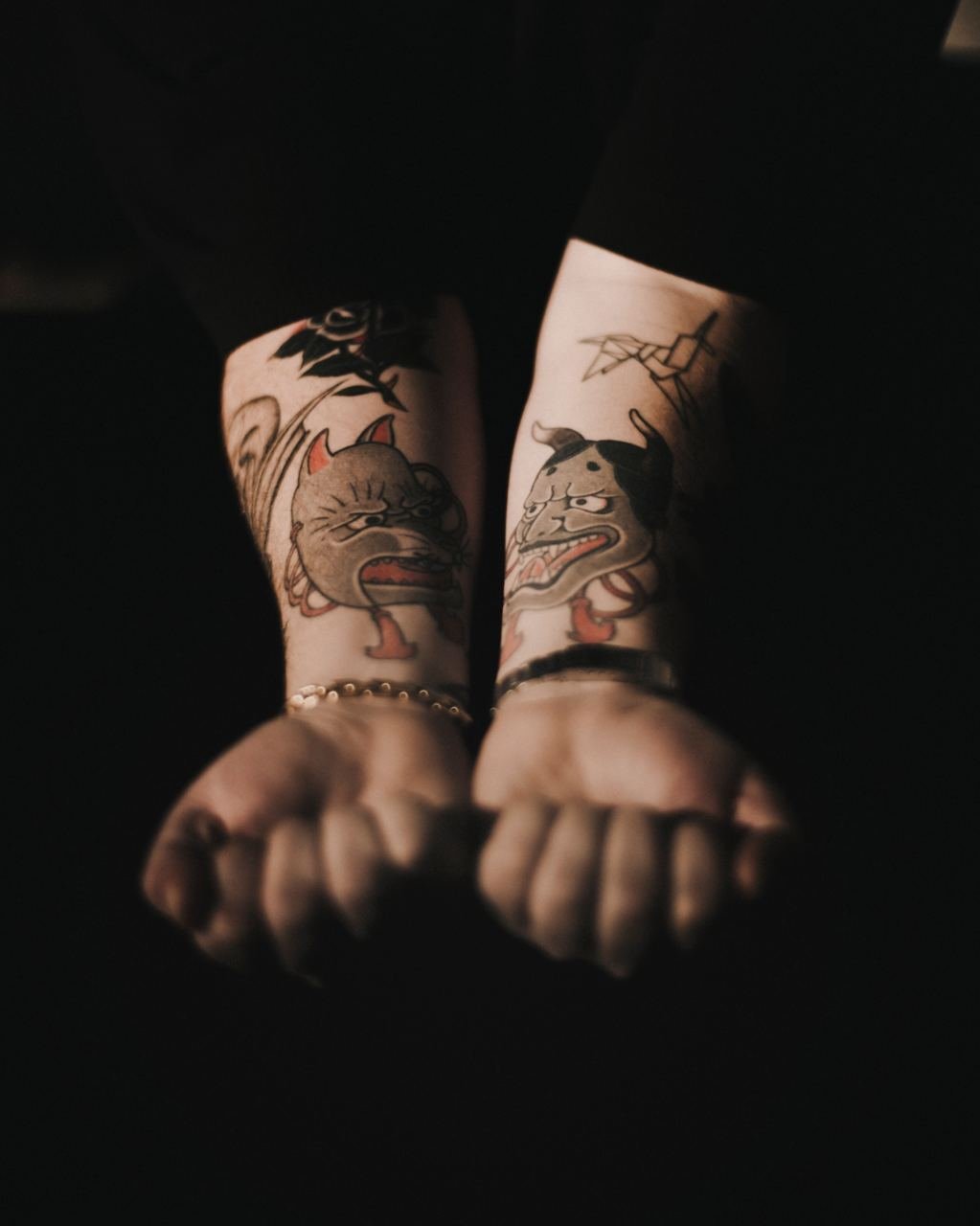 Braccia di una persona con tatuaggi di due gatti e uno di un uccello, visibili i piedi nudi in primo piano.