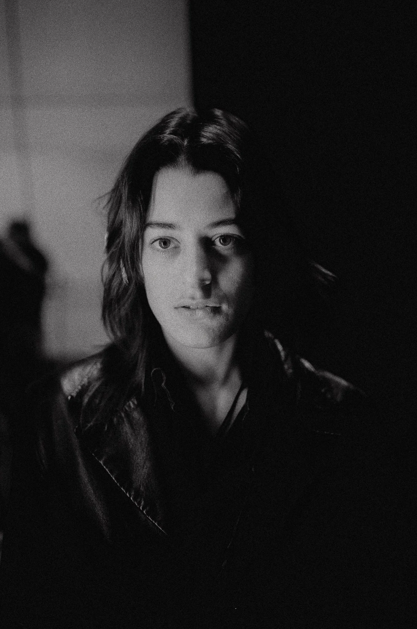 Ritratto in bianco e nero di una donna con capelli lunghi e ricci, con metà viso nascosta in un'ombra.