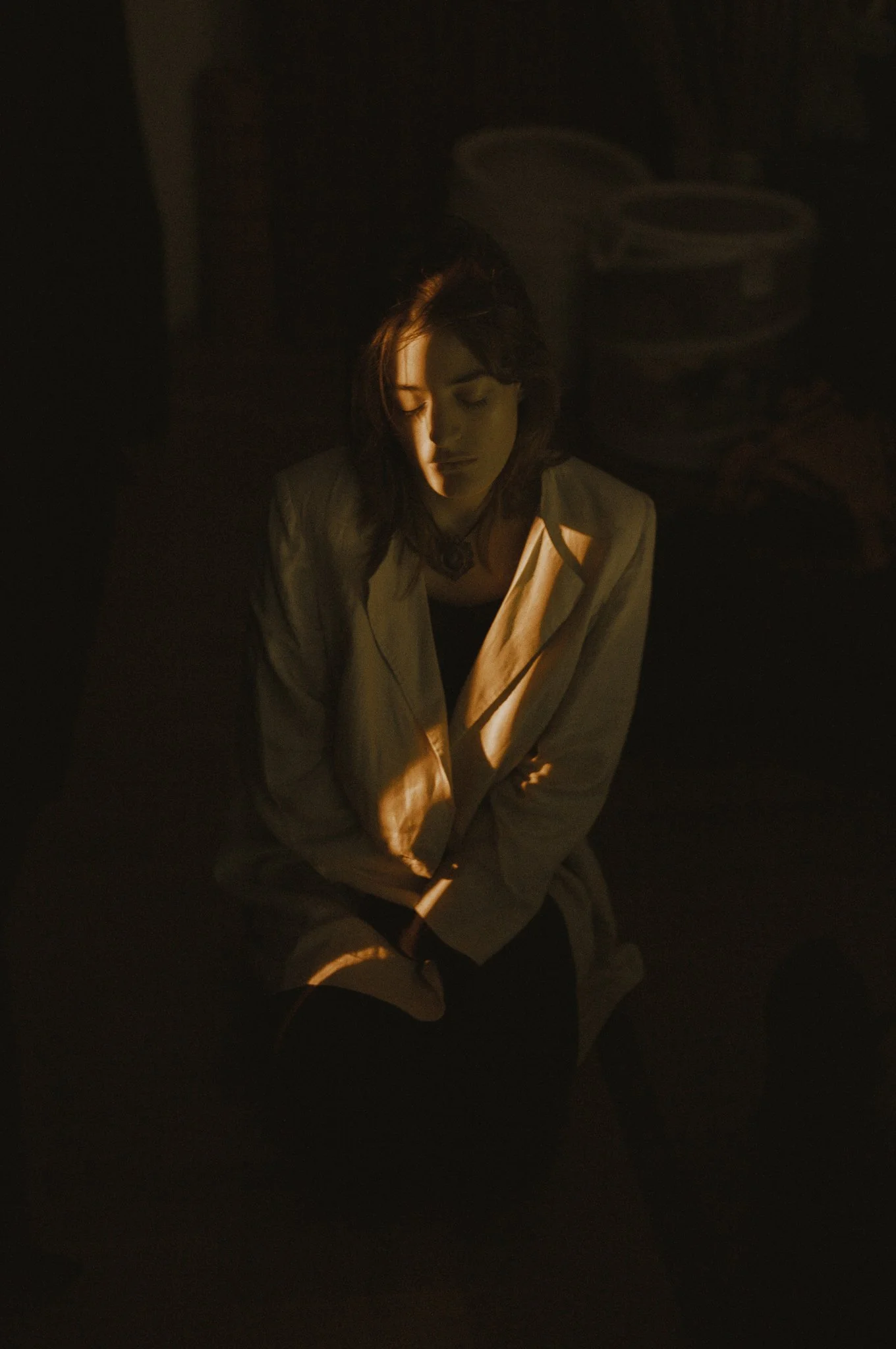 Una donna seduta con i occhi chiusi, illuminata da una luce calda, in un ambiente buio.