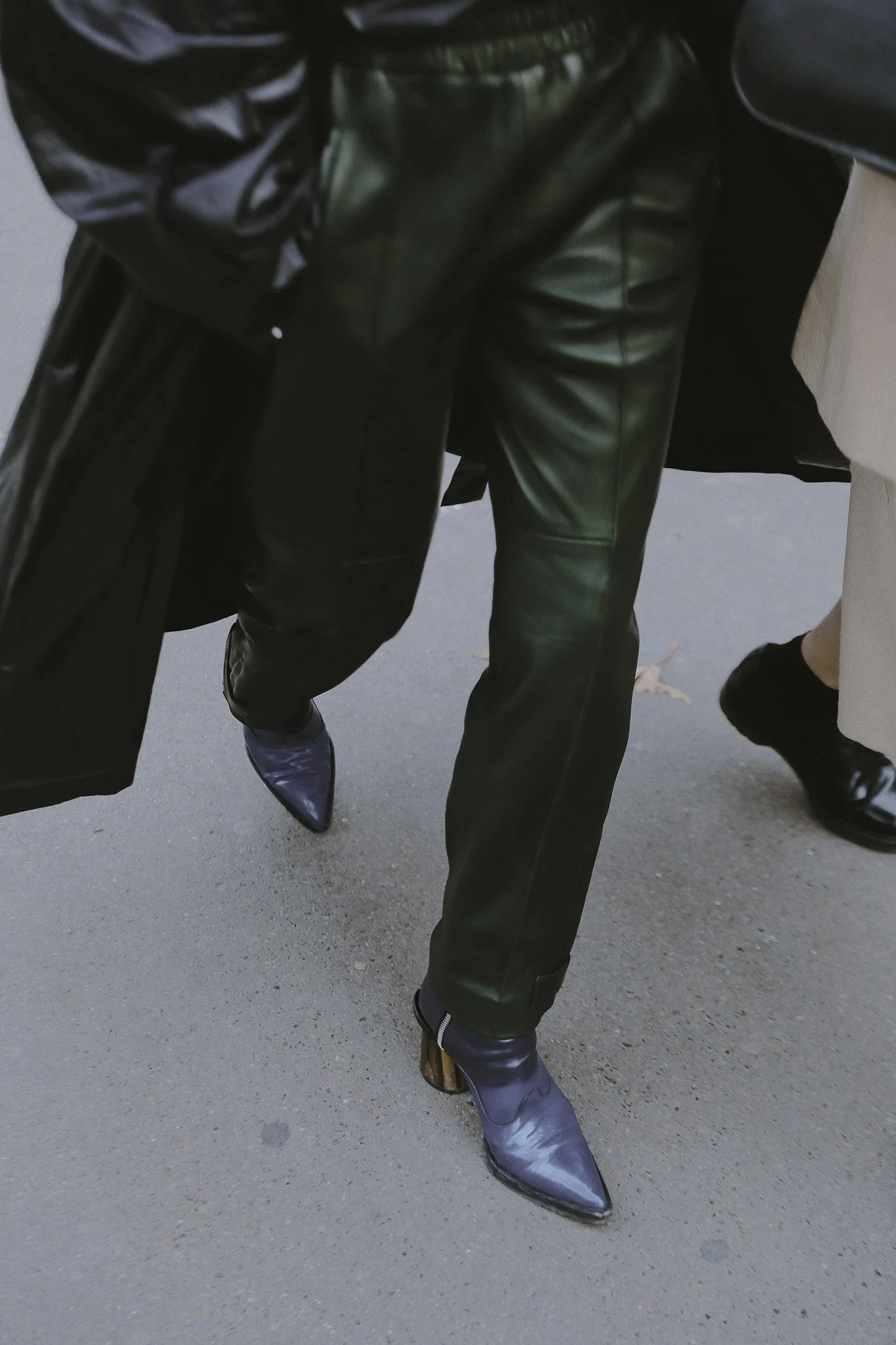 Persone che indossano stivali di diversi stili e colori, con pantaloni di pelle e altri capi di abbigliamento. La scena sembra essere scattata all'aperto su un marciapiede.