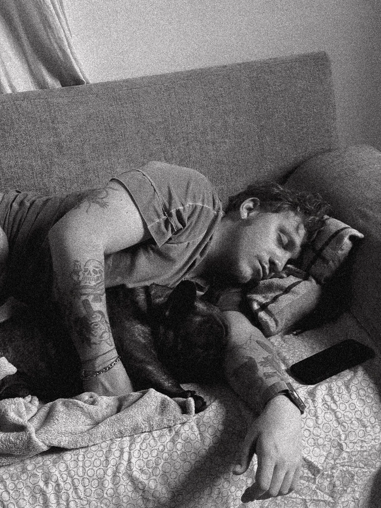 Un ragazzo che dorme sul divano con un cane accanto, entrambi distesi. La scena è in bianco e nero.
