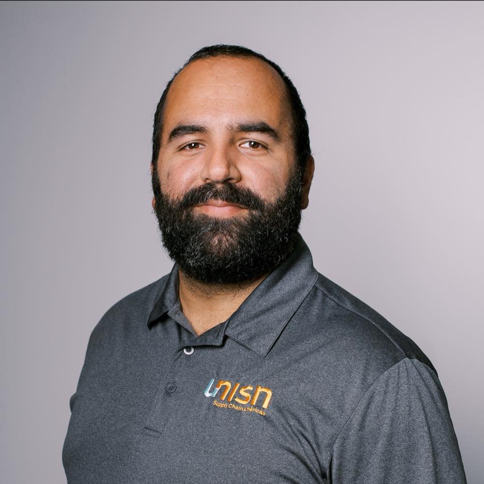 Portrait of a man with a beard, wearing a gray polo shirt with a logo that reads 'UNISN Supply Chain & Services,' standing against a plain light gray background.