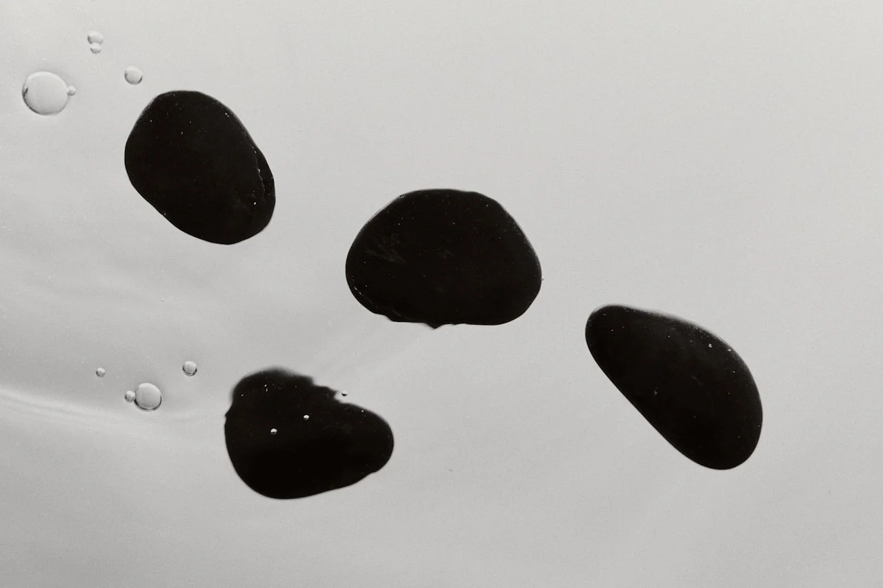 Four black stones floating in water with bubbles around them.