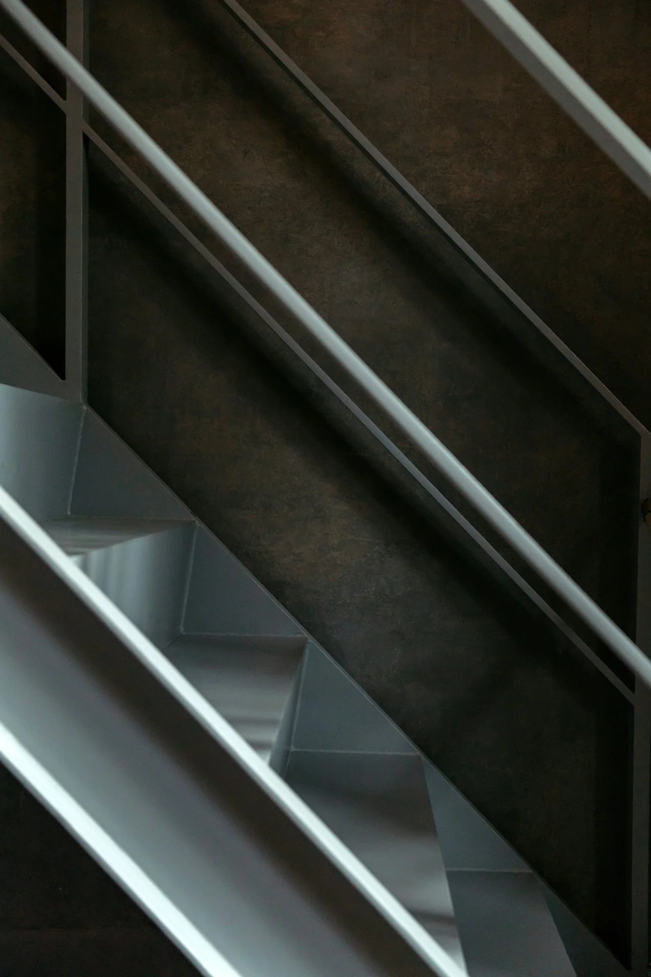 Close-up of a modern metal staircase with dark brown steps and silver handrails.