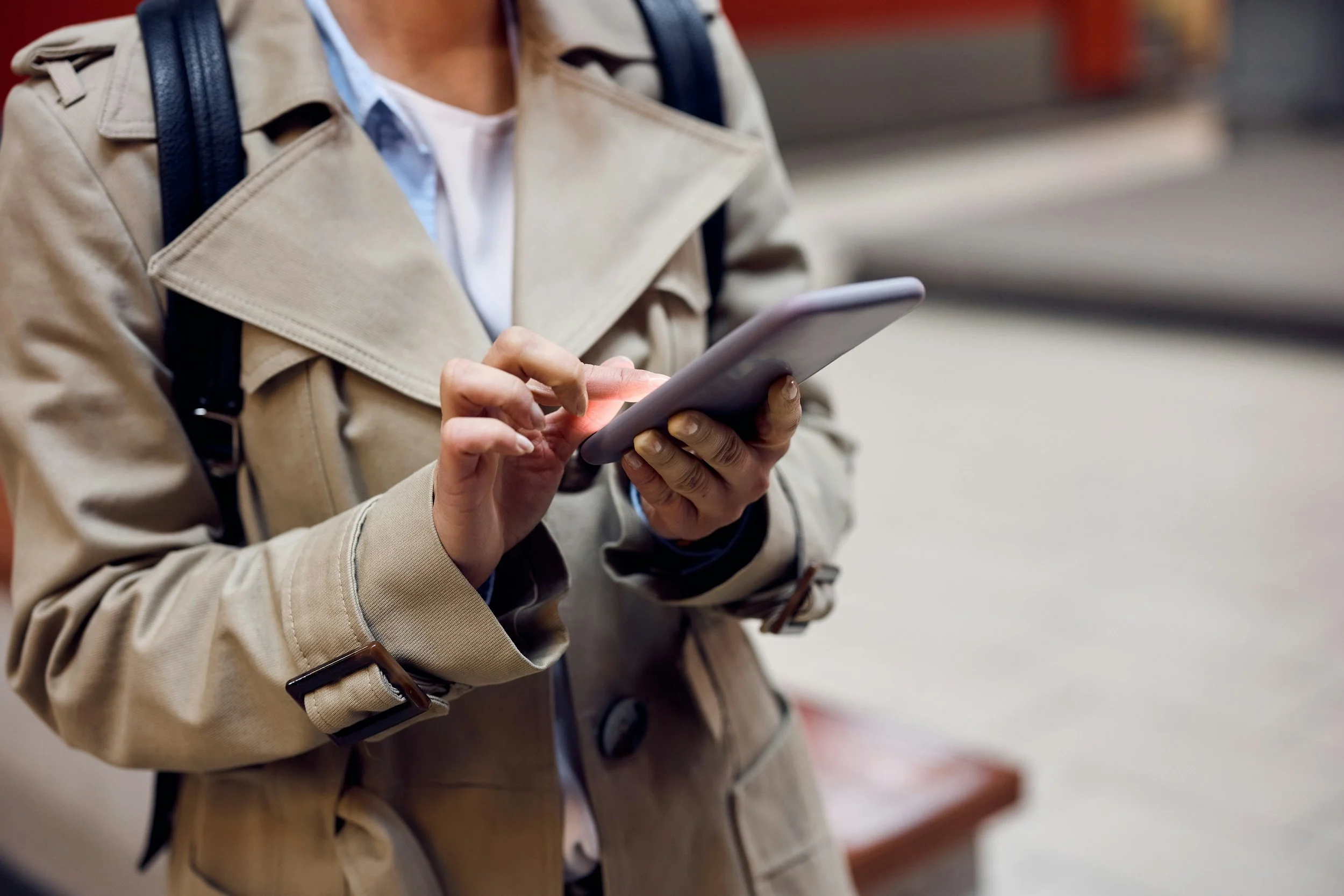 Person in a beige trench coat using a smartphone outdoors.