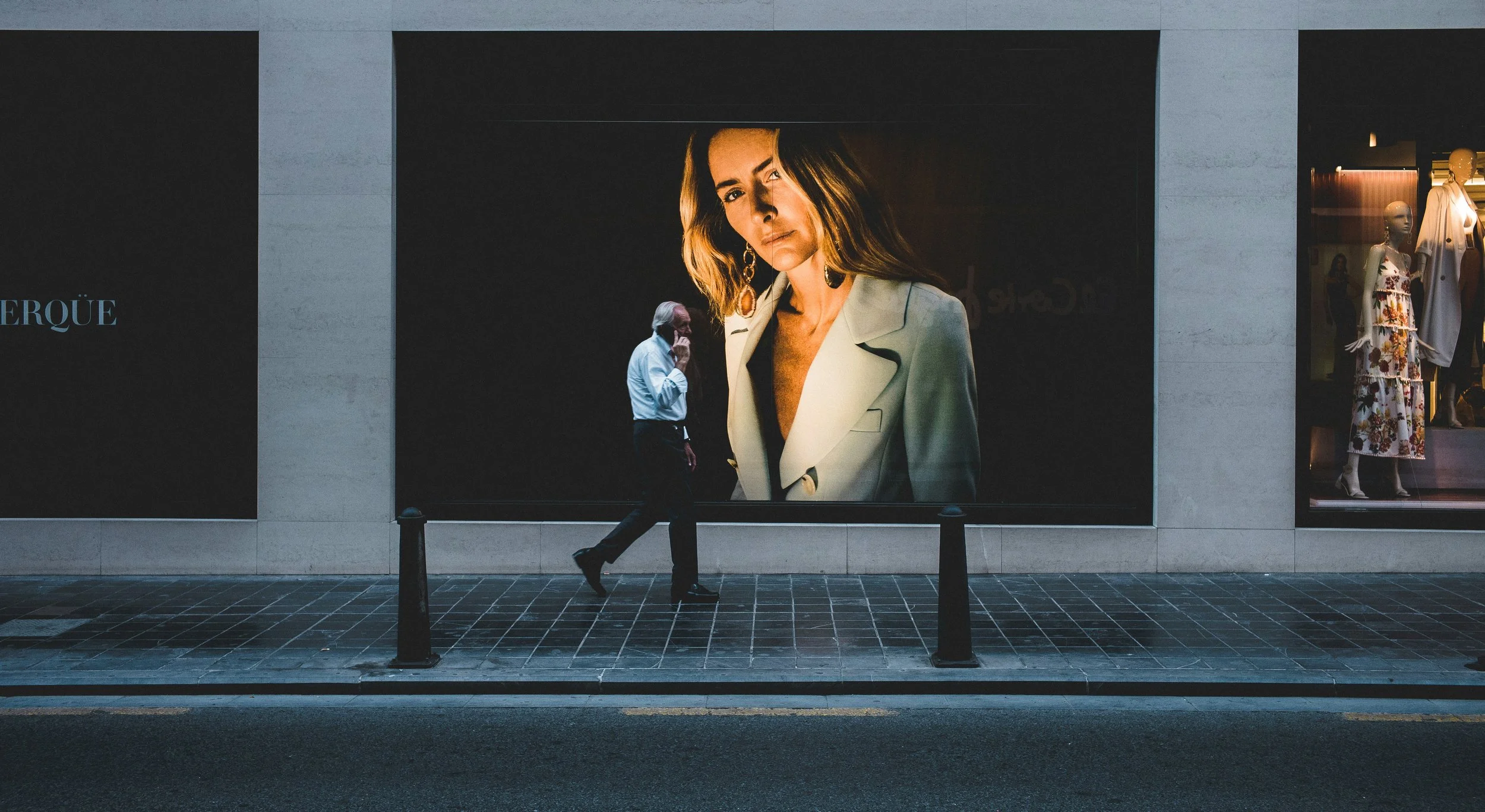 A man walking on the sidewalk past a large advertisement featuring a woman in a cream-colored jacket.