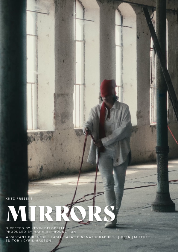 Une femme portant une veste blanche, un pantalon blanc et un foulard rouge couvre-œil marche dans un espace industriel abandonné avec de grandes fenêtres. Elle tient une corde.