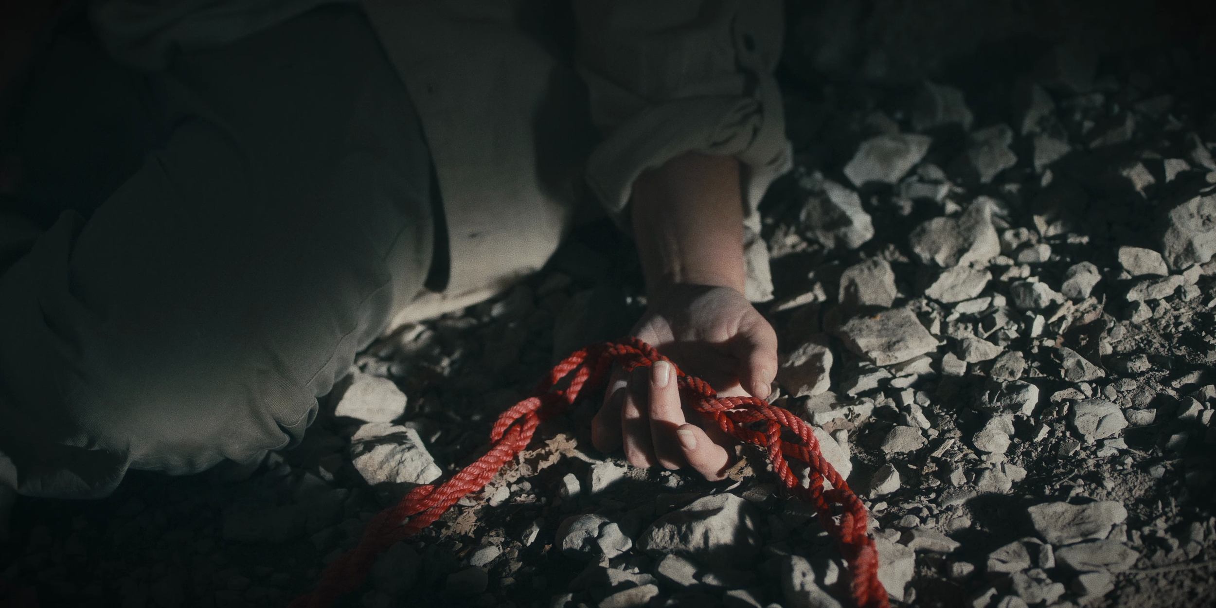 Une personne allongée sur le sol rocailleux, tenant une corde rouge dans sa main.