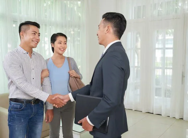 Two young adults shaking hands with a professionally dressed man holding a folder, helping them with their health insurance needs.