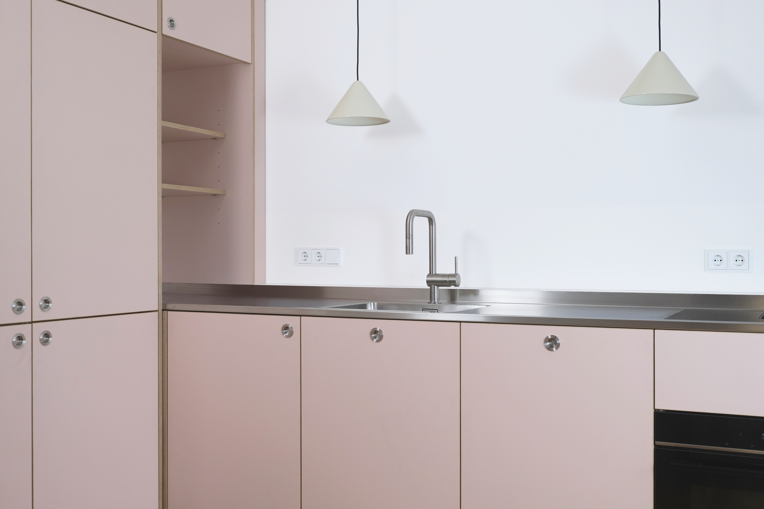 Ansicht einer modernen Küche mit pinkfarbenen Schränken, einer Spüle, einem Wasserhahn und zwei weißen Pendelleuchten.