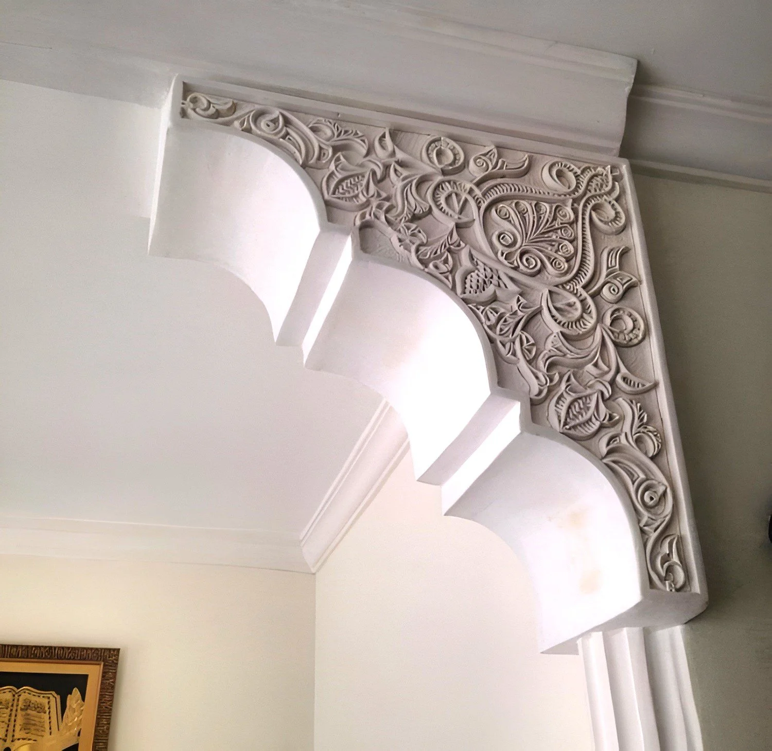 Decoratieve witte gipskroonlijst met ingewikkeld reliëf en bloemmotieven onder de plafondrand in een interieur.