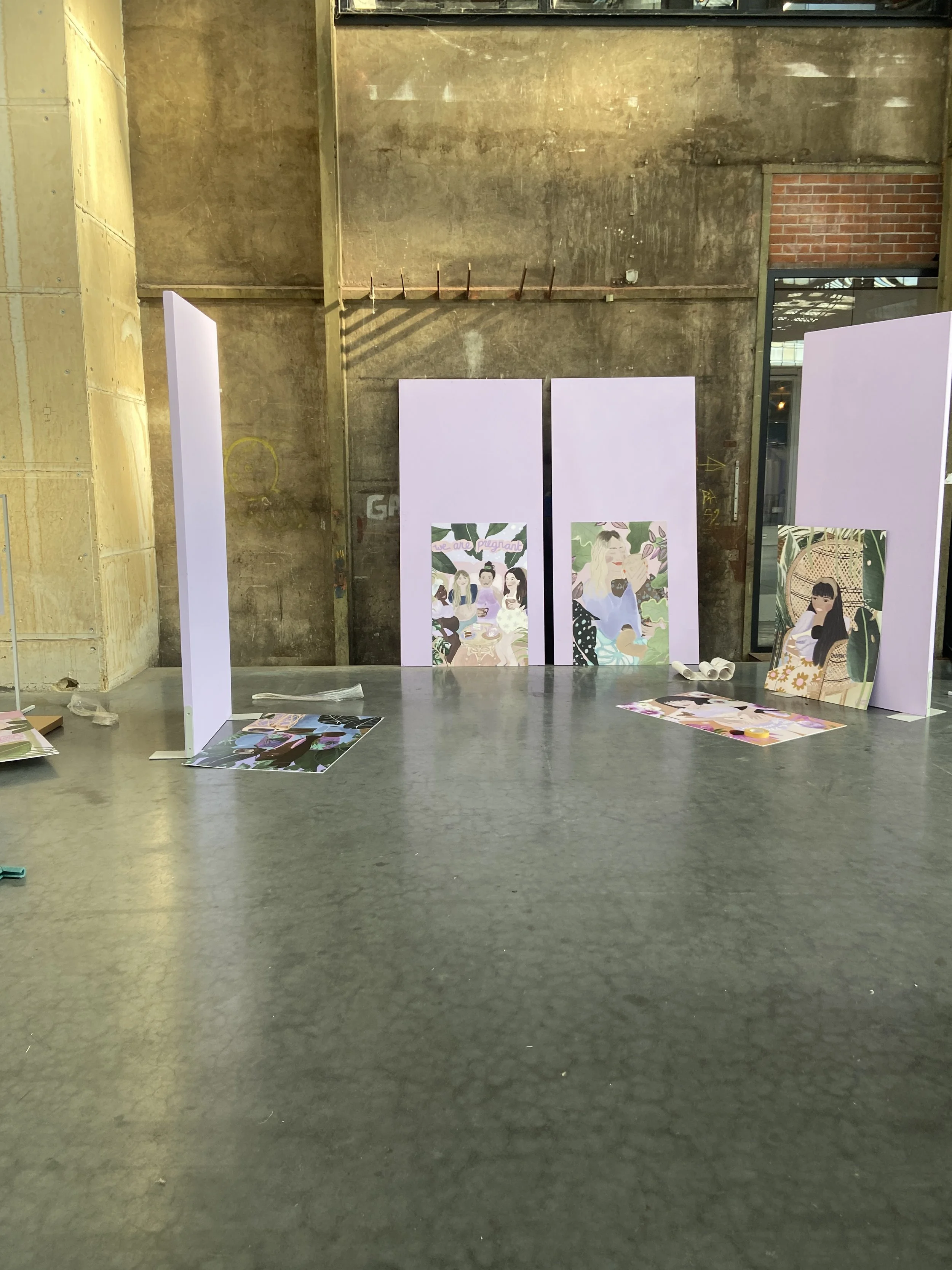Interior of a room with unfinished walls, featuring posters and artwork on the floor and leaning against the wall, some of which depict women and illustrations of plants, flowers, and nature.