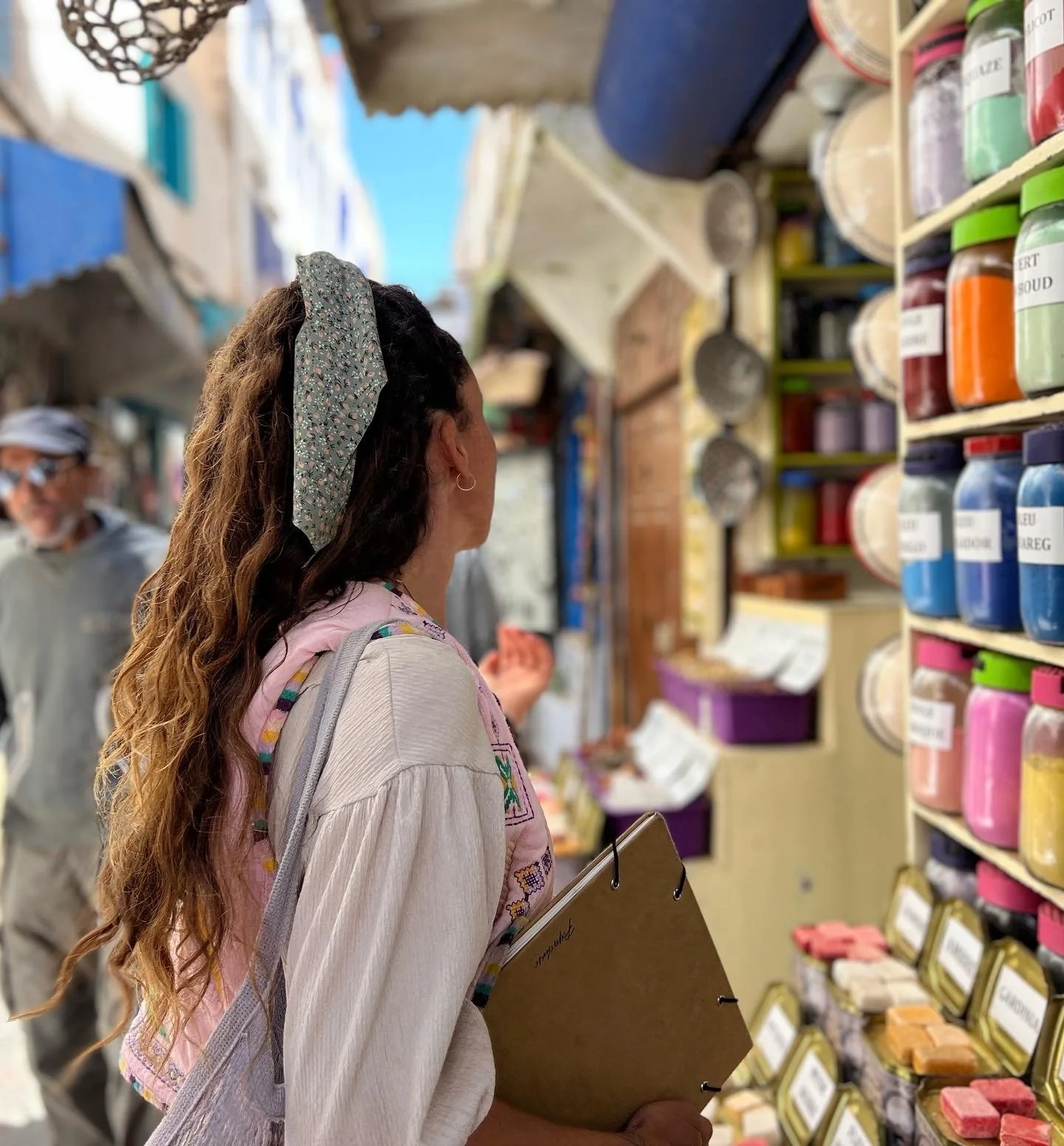 Woman shopping at a store, looking at colorful products on shelves, with a man in the background.