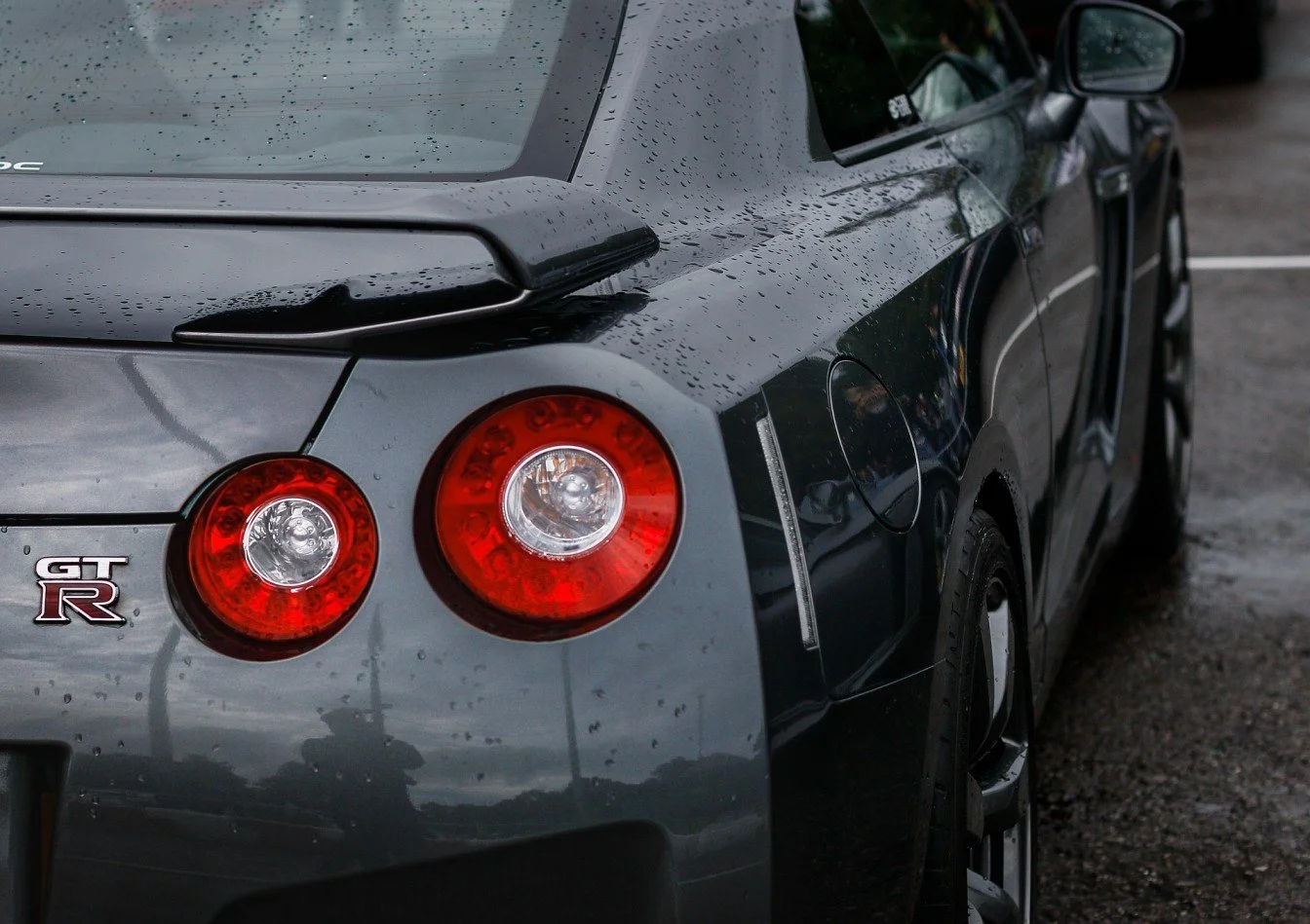 Rear view of a gray Nissan GT-R sports car with water droplets on the surface, parked on a wet road.