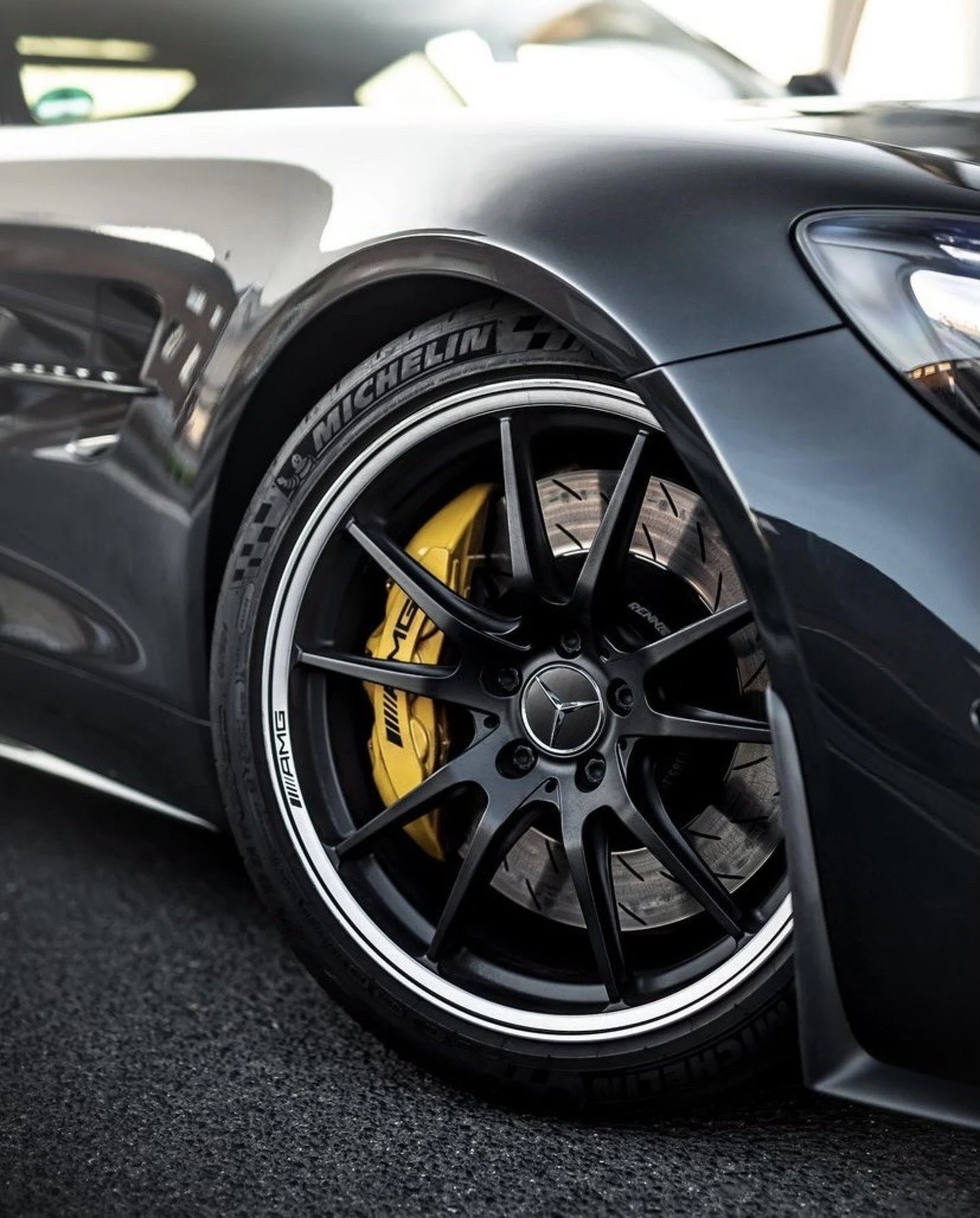 Close-up of a high-performance sports car's front wheel, showing black rims with Mercedes-Benz emblem, yellow brake caliper, and Michelin tire.