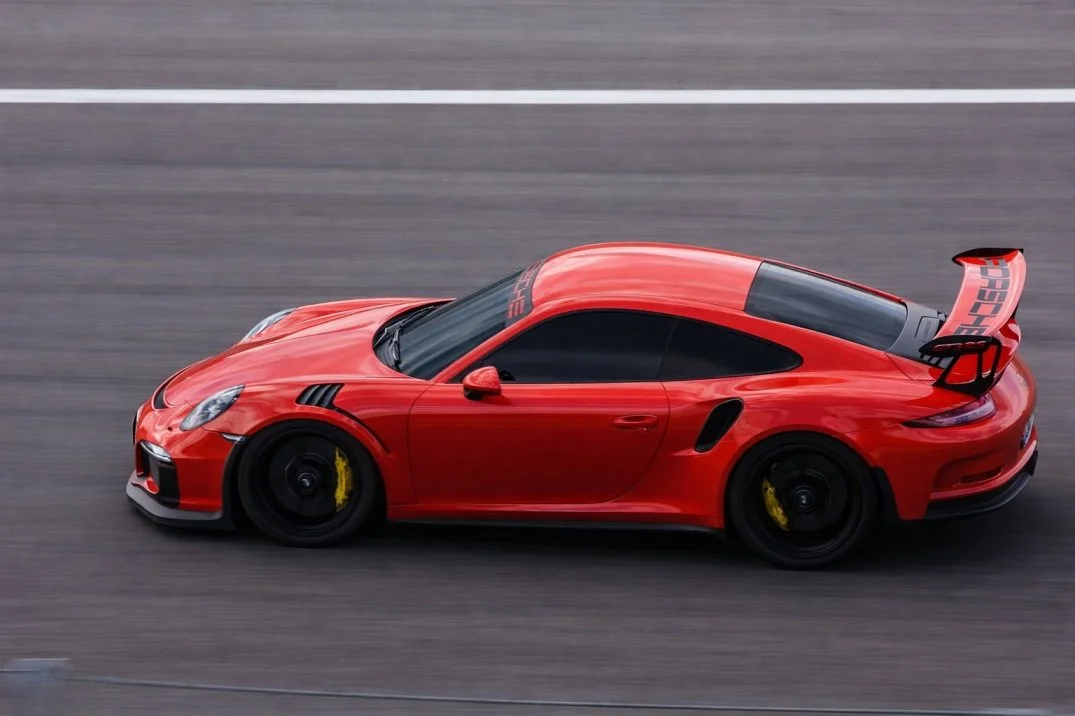 Red Porsche sports car with a rear wing on a racetrack.