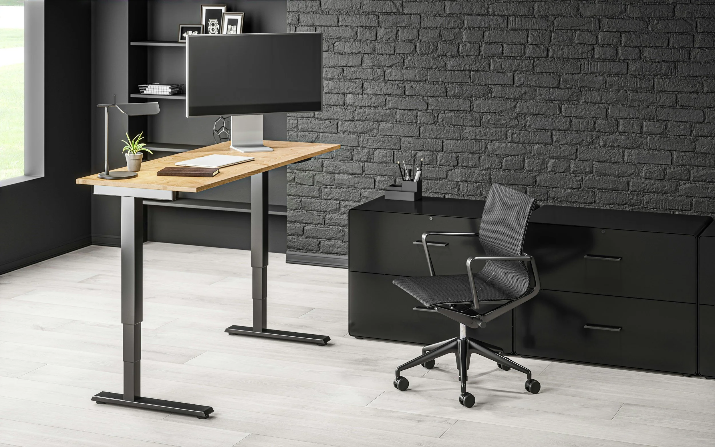 Modern home office with a standing desk, swivel chair, gray brick accent wall, black storage cabinet, and desktop accessories.