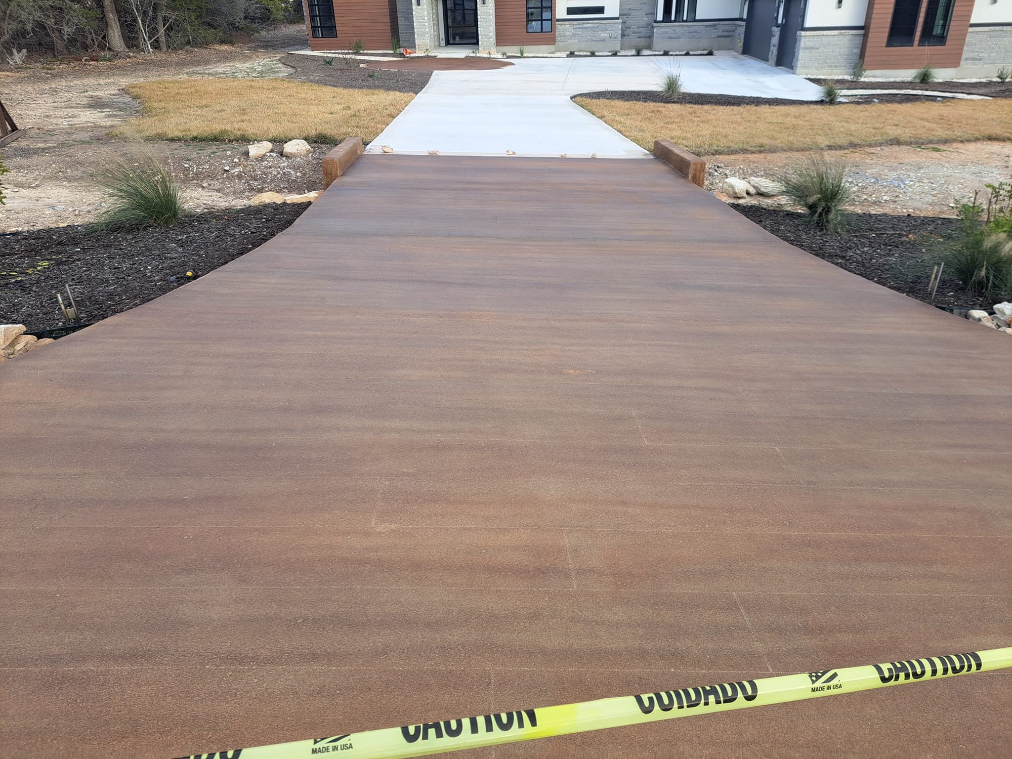 Newly constructed cement and wooden walkways leading to the entrance of a house, with landscaping and caution tape in the foreground.