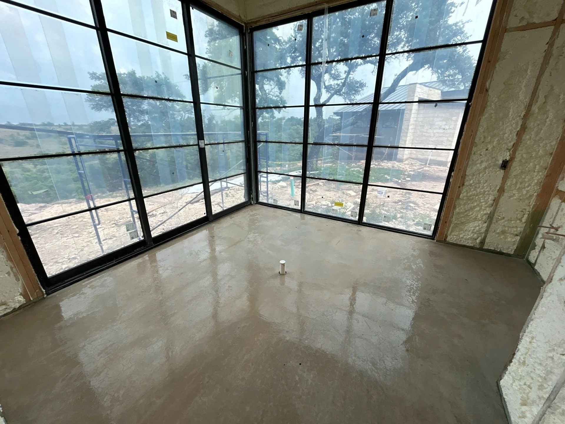 Empty room with large window walls, construction in progress, with concrete floor and insulation walls.