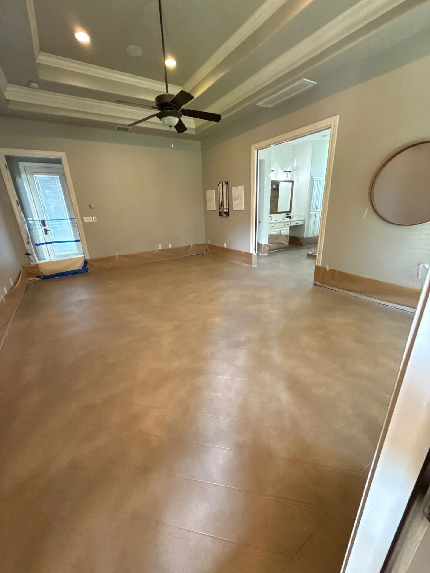 Empty room with a ceiling fan, light fixtures, a door leading to a balcony, and a doorway to a bathroom, with tan colored flooring and beige walls.