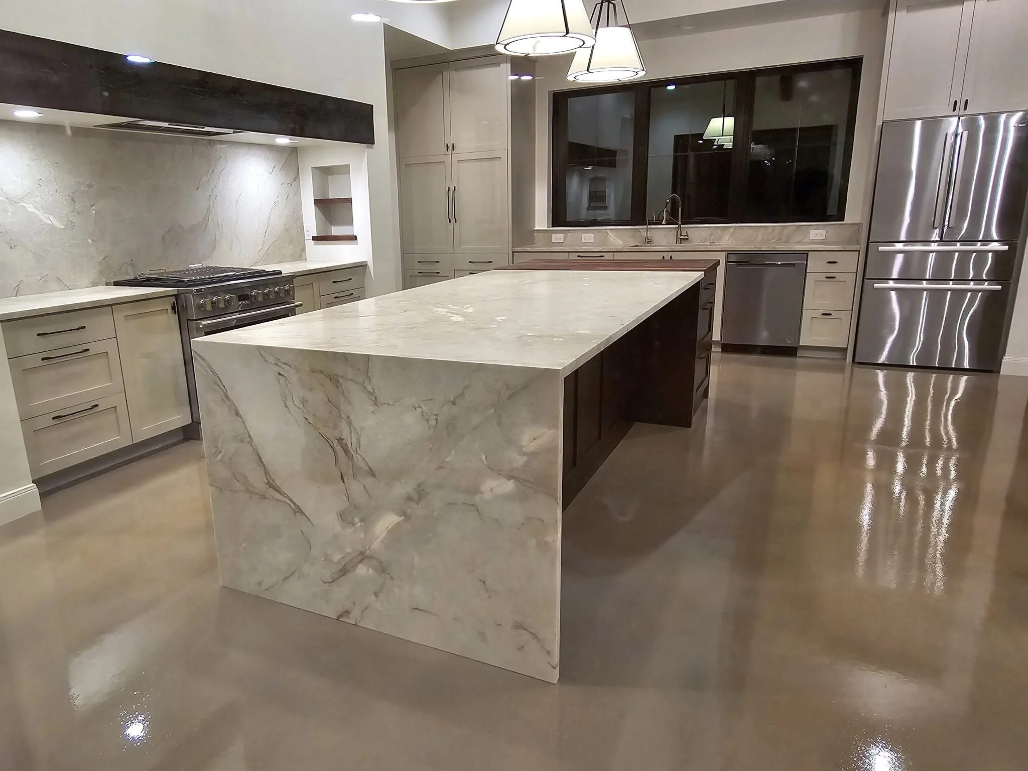 Modern kitchen with marble countertops, an island, stainless steel appliances, and beige cabinets.