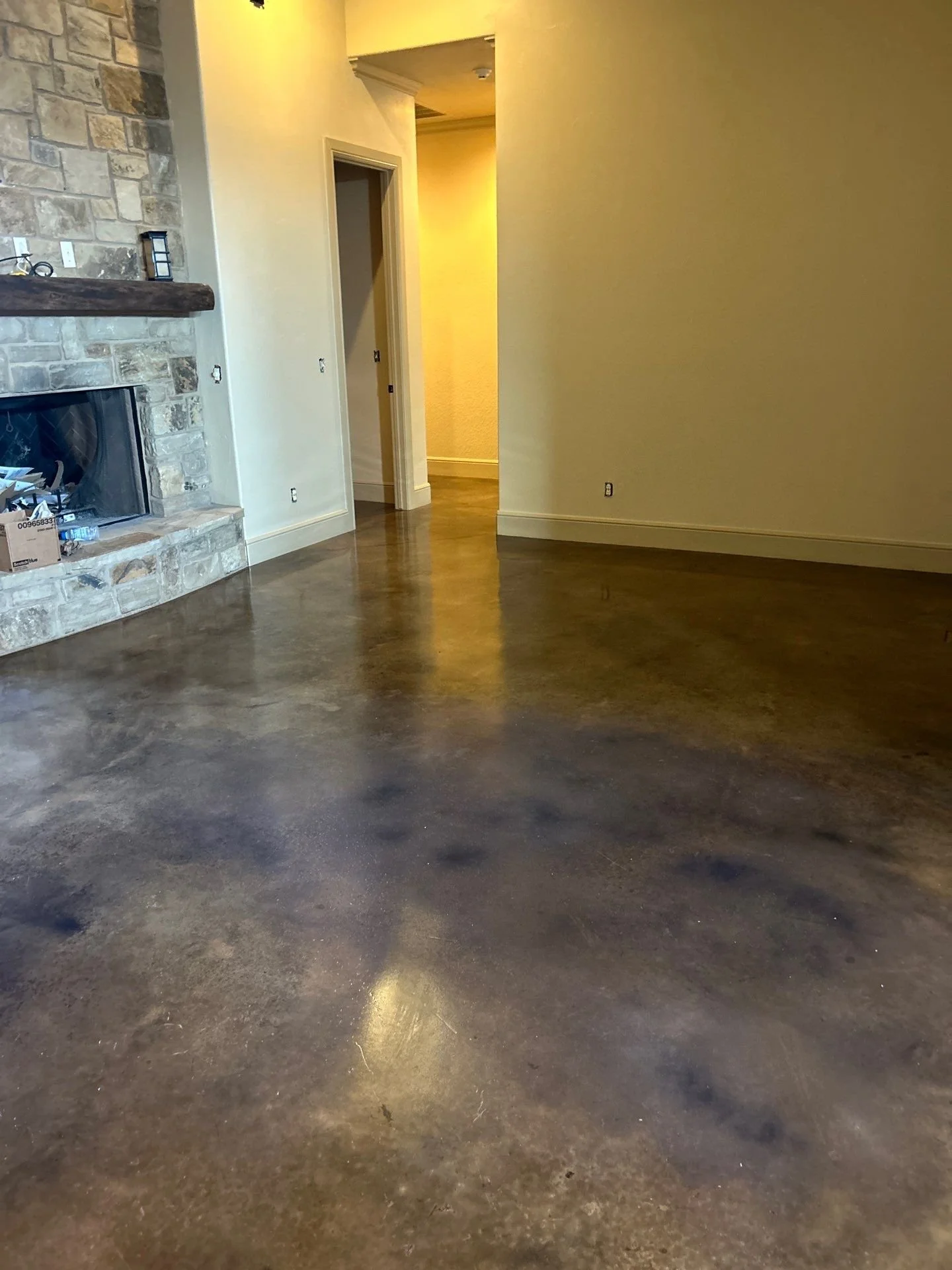 Empty living room with a polished concrete floor, a stone fireplace, and a doorway leading to another room. The walls are painted yellow and beige.